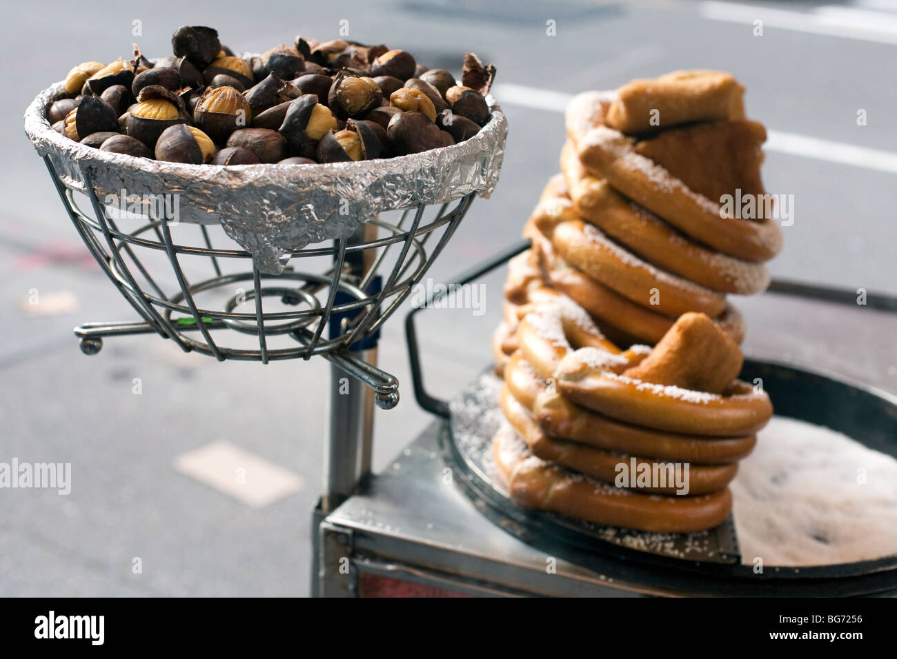 a pan of tempting roast chestnuts & a pile of golden pretzels displayed on a vendors cart on Fifth Avenue NYC Stock Photo