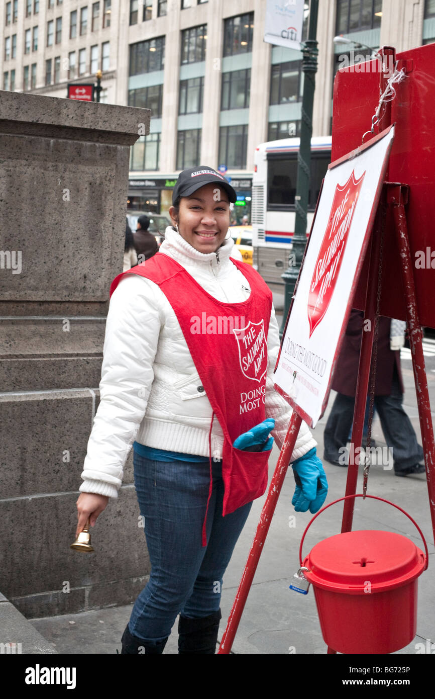 black Salvation Army bell ringer working the corner of Fifth Avenue & 42nd Street with a big smile & red bucket for donations NY Stock Photo