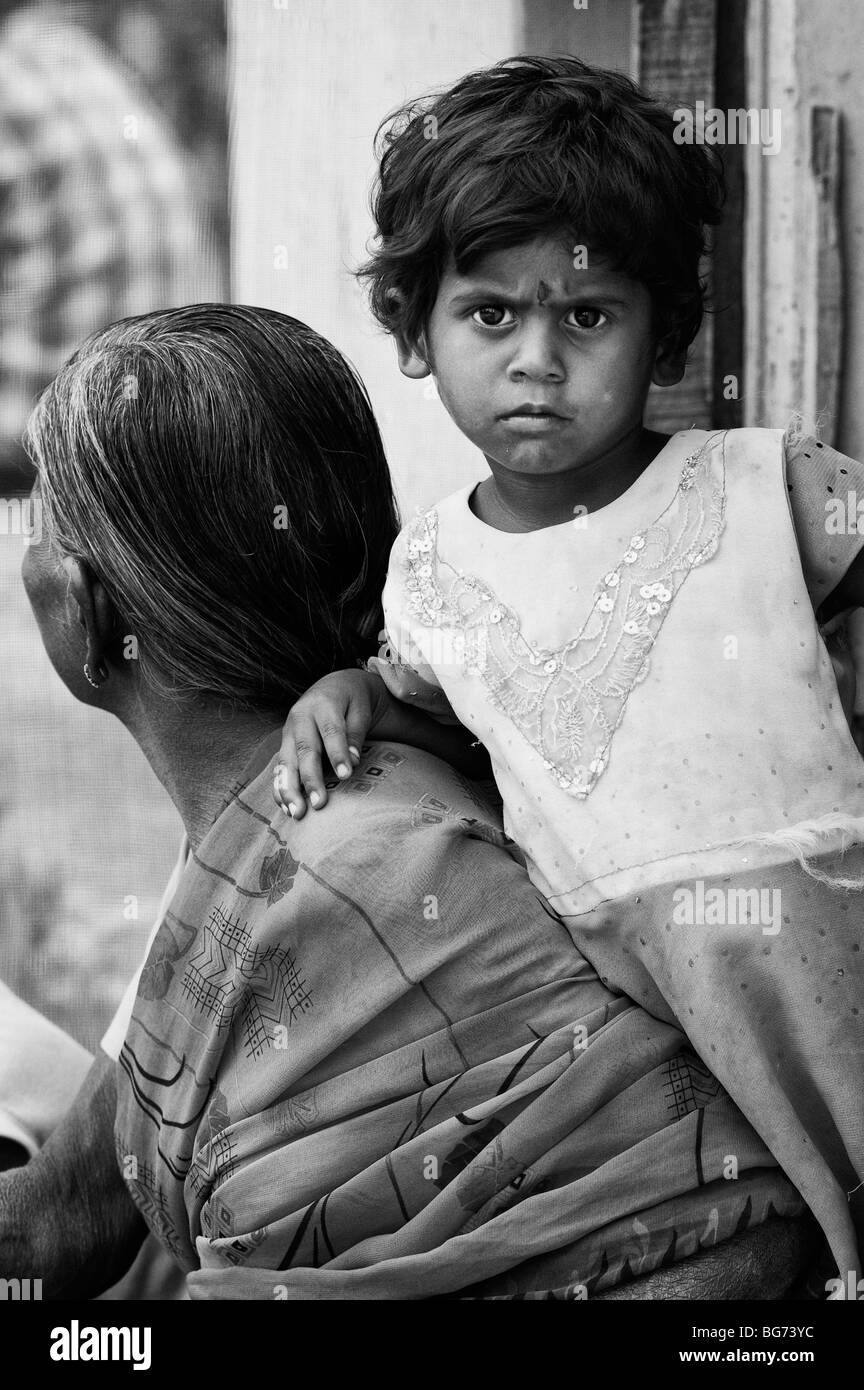 Indian toddler leaning on her grandmother in the doorway of there house in a rural indian village. Andhra Pradesh, India. Monochrome Stock Photo