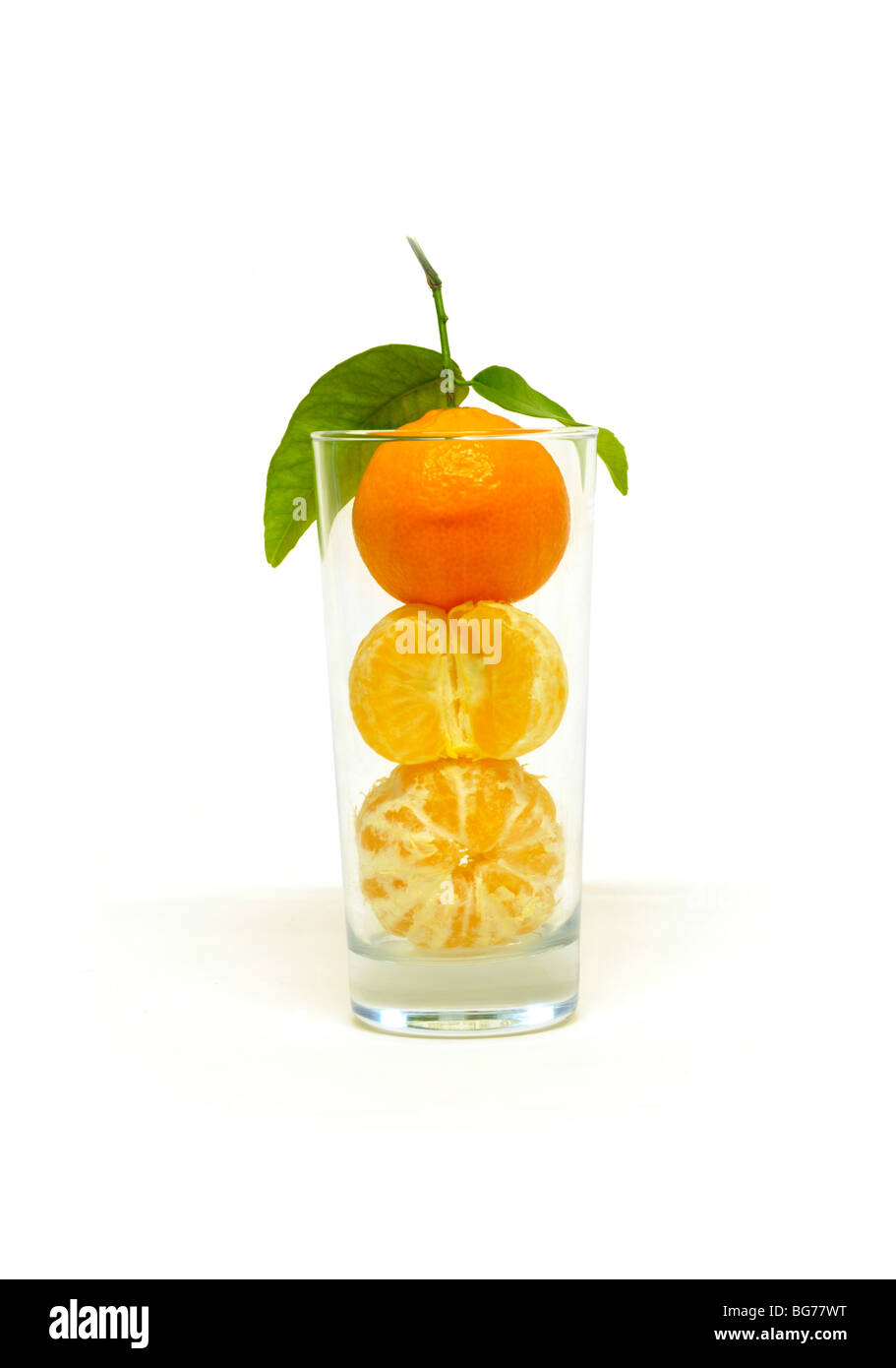 Whole peeled and unpeeled oranges stacked on one another within a glass tumbler. Stock Photo