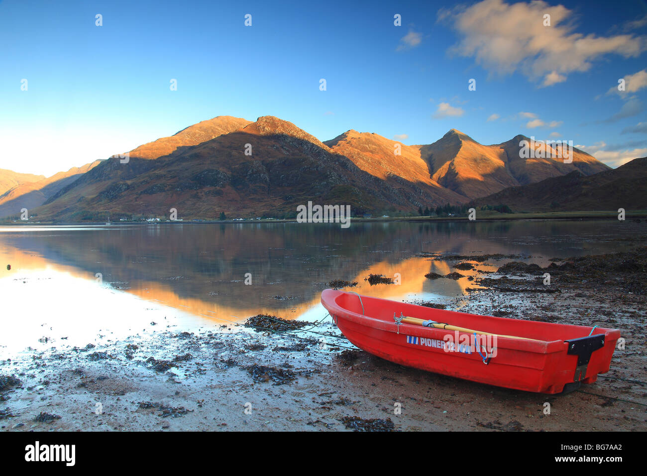 Landscape of a red rowing boat on the shoreline of Loch Duich, Scotland with the Five Sisters mountain range in the background. Stock Photo