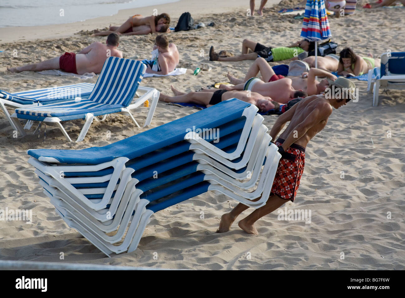 BEACH LIFE, LOUNGERS, WORKERS: A man taking away loungers end of day at  Sitges famous gay beach resort near Barcelona Spain Stock Photo - Alamy