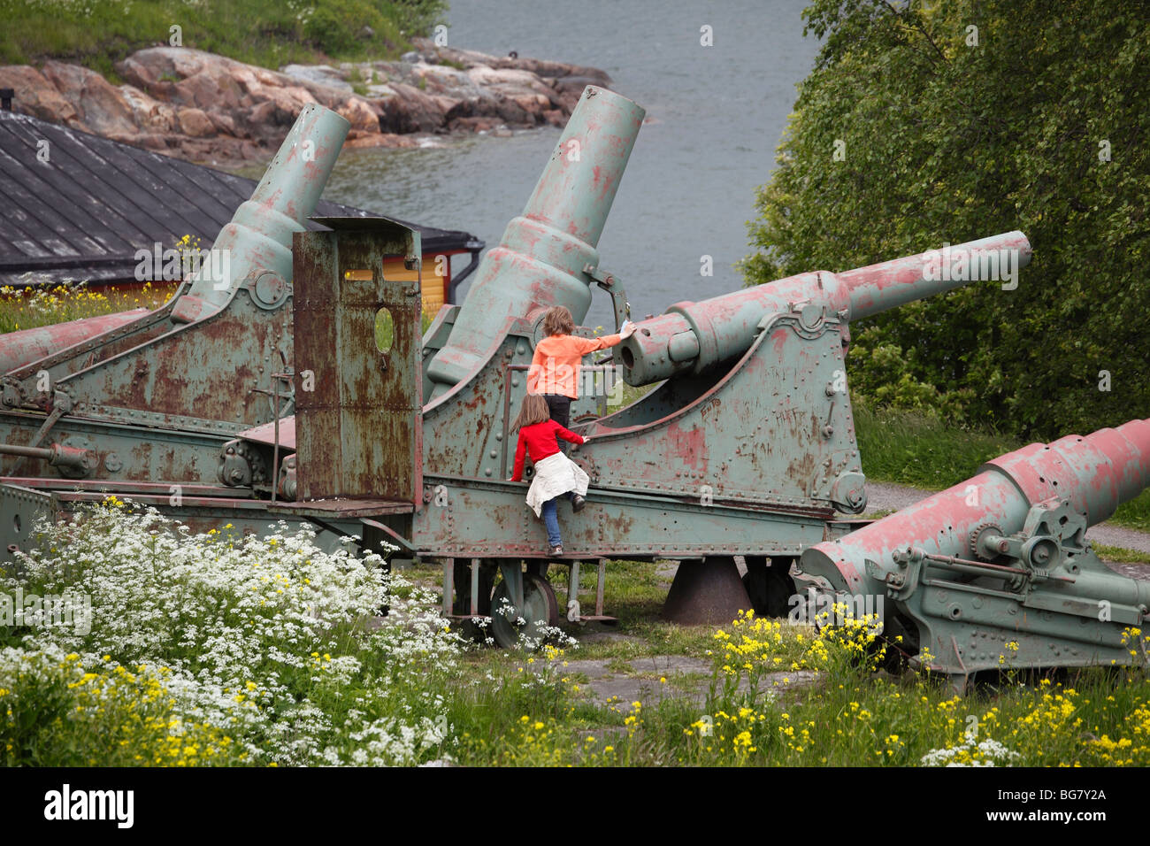 Finland, Helsinki, Helsingfors, Suomenlinna Island, Kustaanmiekka, Children Playing at Historic Cannon, Wild Flowers Stock Photo