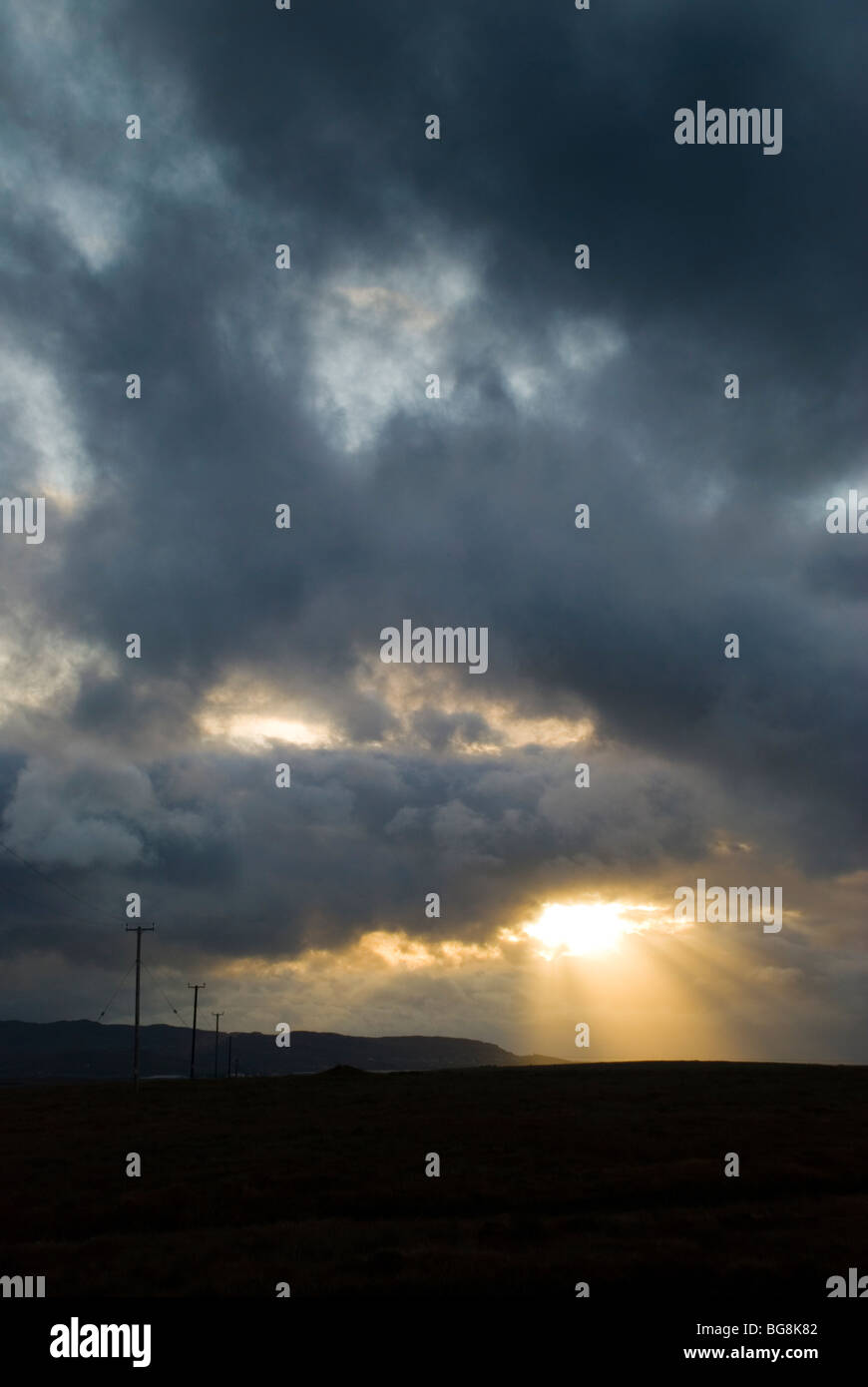 Electricity cables march across the bogland as sun bursts through stormclouds in rural Ireland Stock Photo