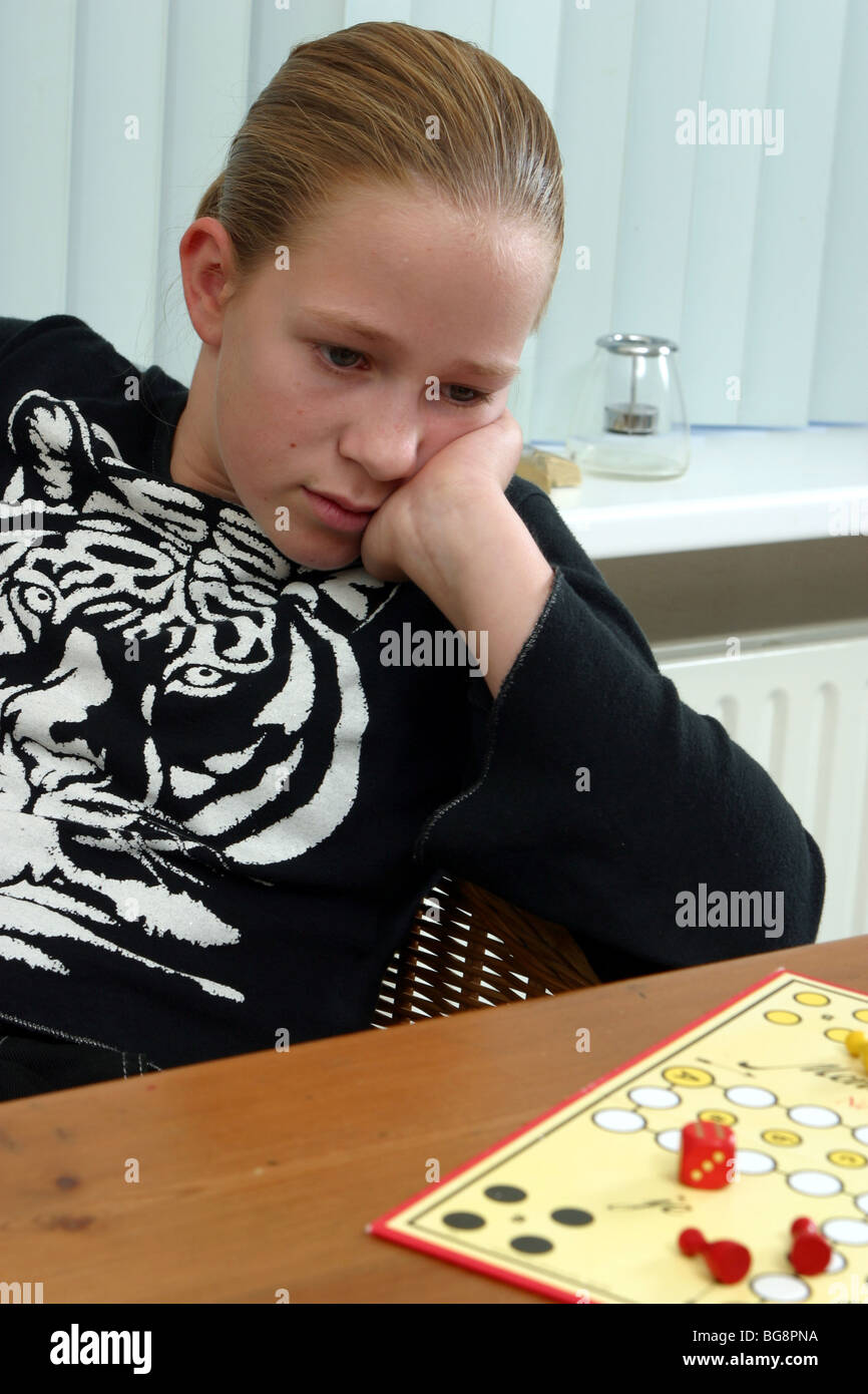 Unhappy preteen child looking annoyed at the board game Mensch ärgere dich nicht on the table,might be defeated or feeling alone Stock Photo