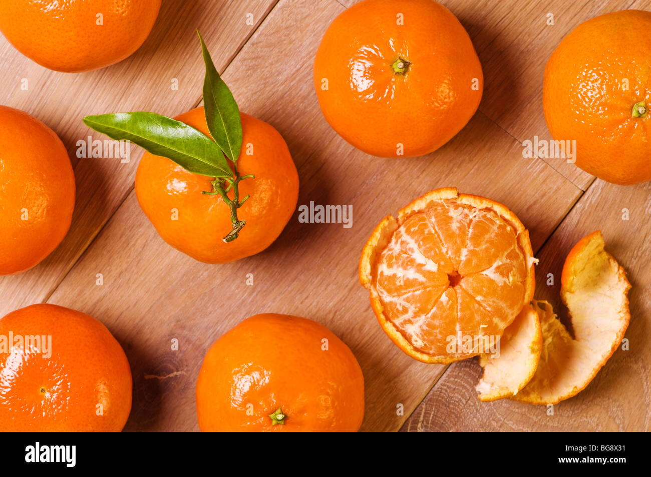 Overhead view of clementine fruits, one with leaves and one half peeled