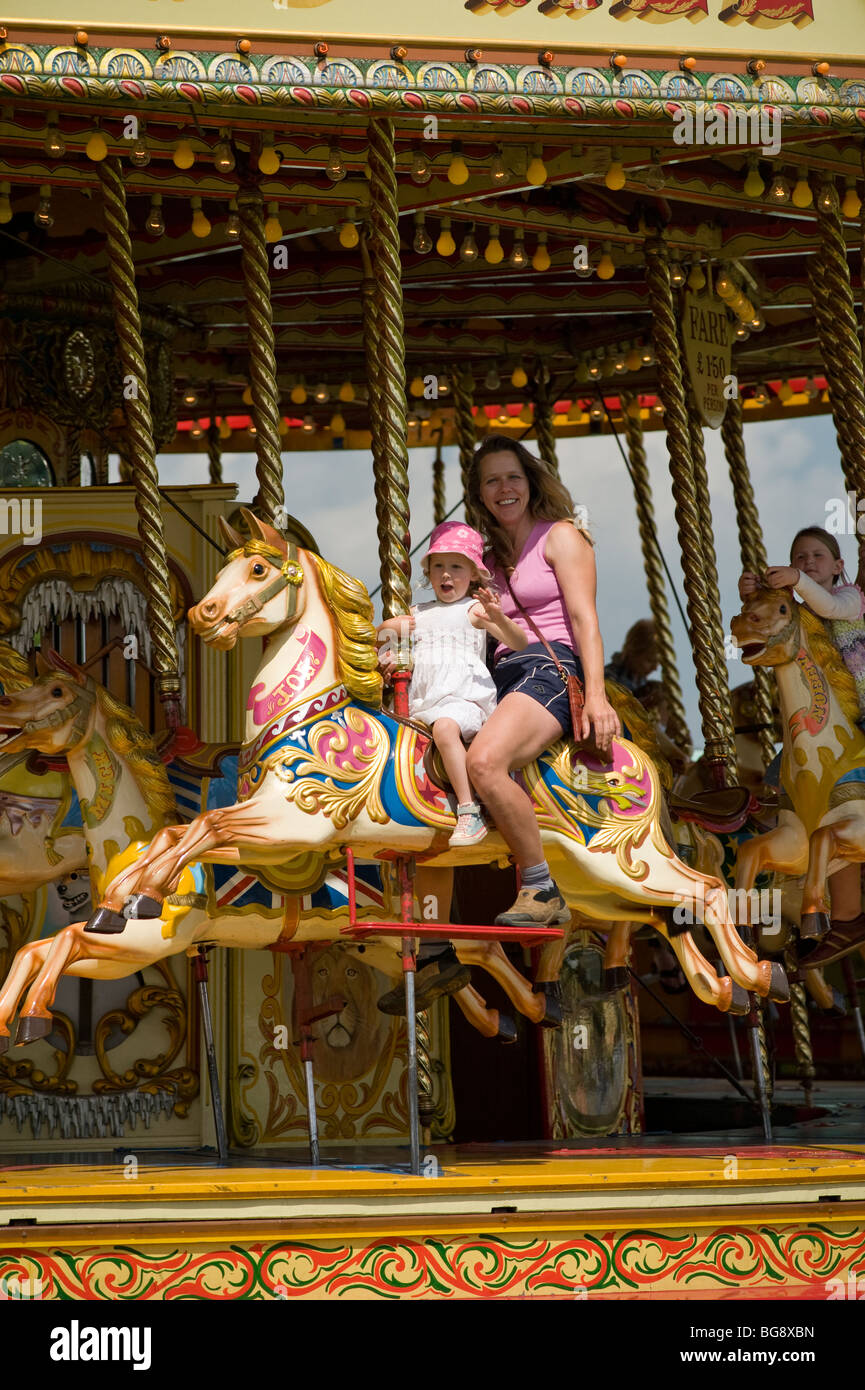 smiling mother and small daughter riding together on fairground steam galloper roundabout Stock Photo