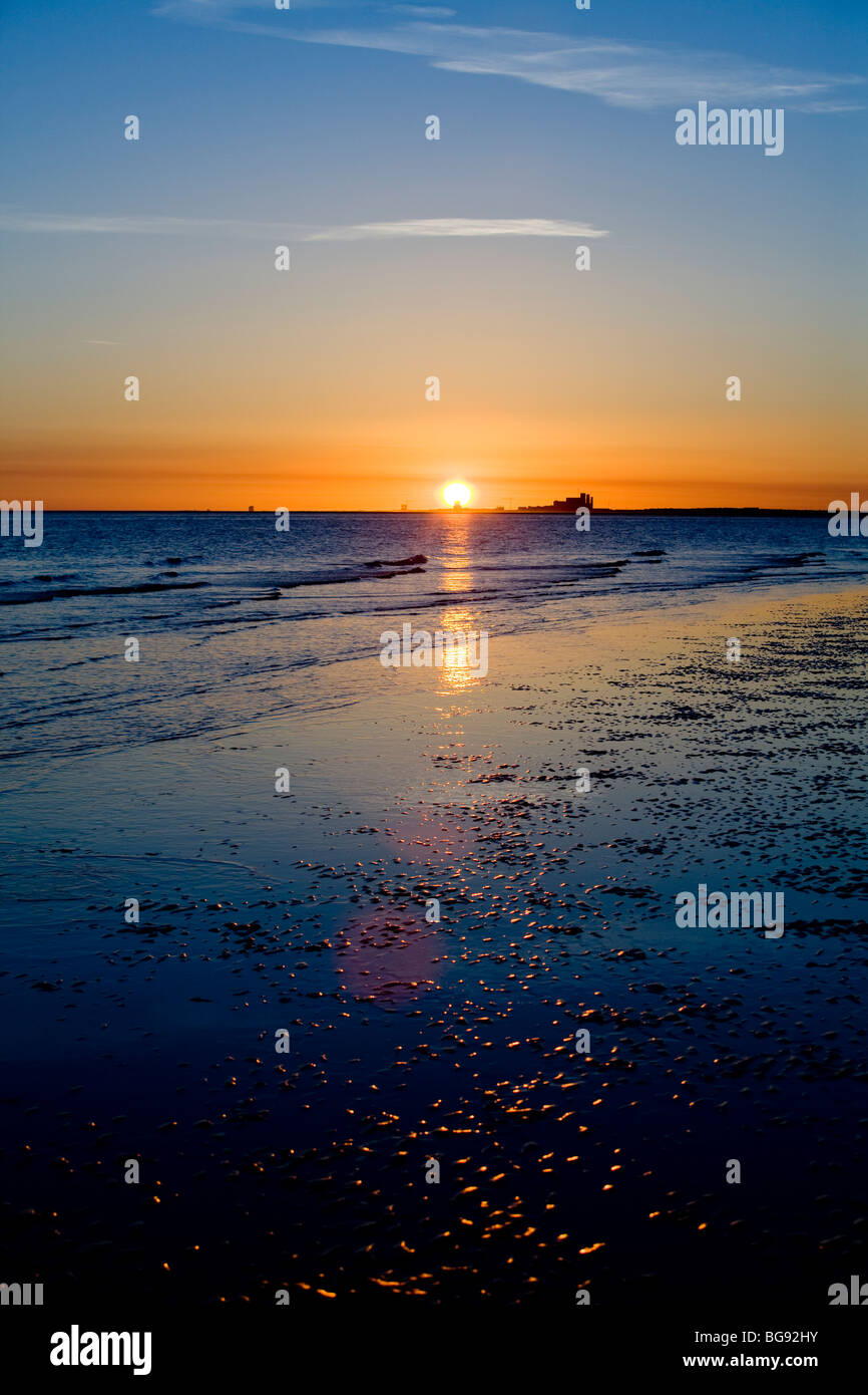 Light twinkles on a beach during sunset or sunrise over an ocean. Stock Photo