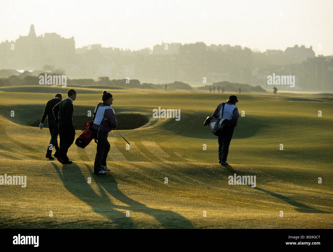 Golfers and their caddies crossing a golf course Stock Photo Alamy