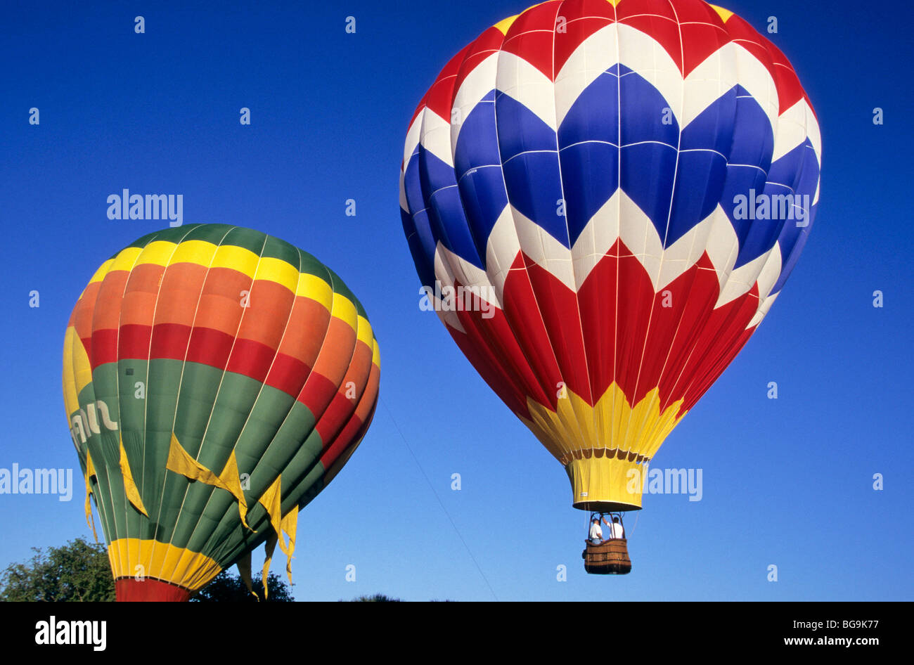 Two brightly coloured hot air balloons rising from the ground Stock