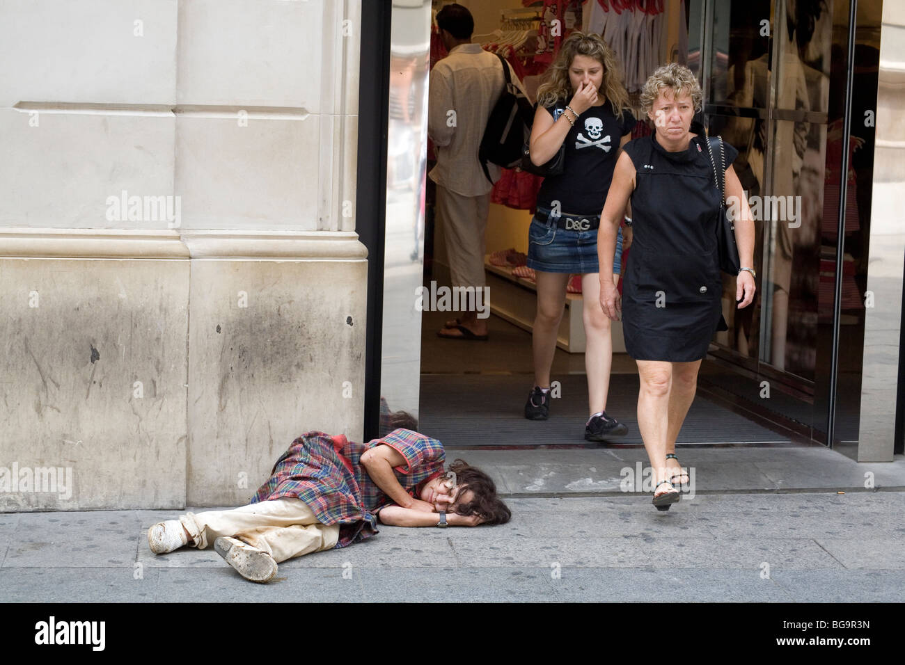 WOMAN HOLDING NOSE, HOMELESS PERSON, BARCELONA: Shopper holds nose – homeless woman asleep outside upmarket boutique Passeig de Gracia Barcelona Spain Stock Photo