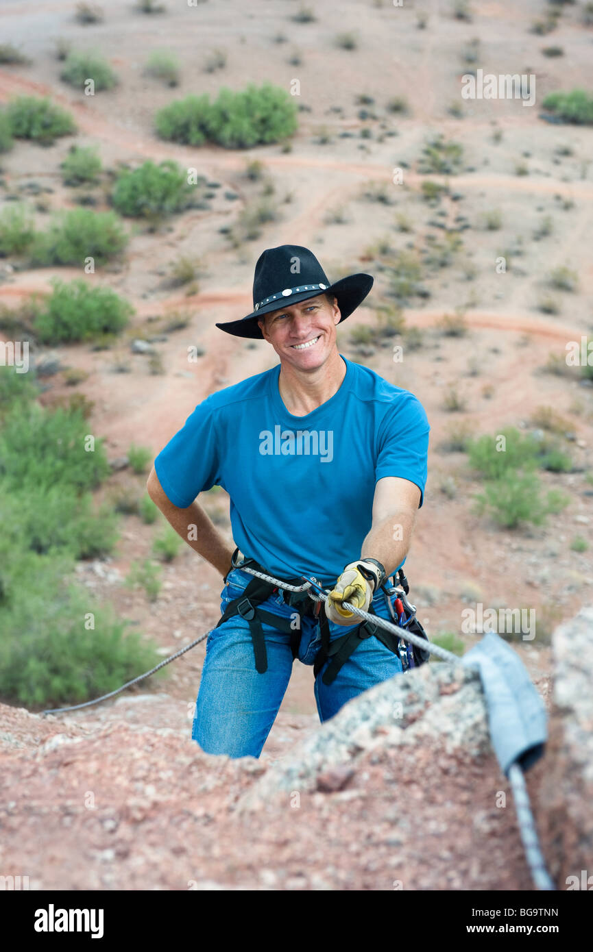 A close up of a smiling rock climber getting ready to rappel down a mountain after a climb up a steep slope. Stock Photo