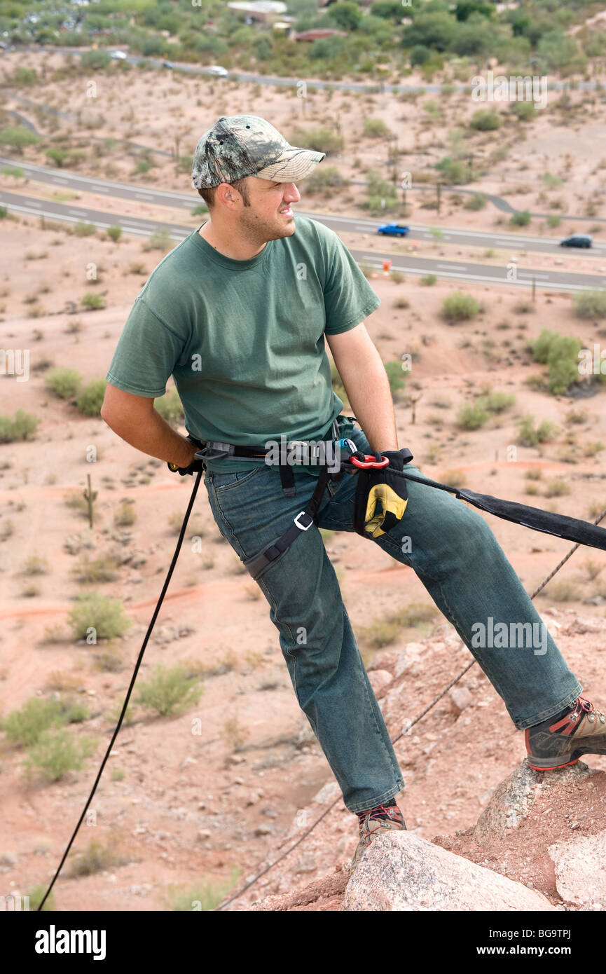 A rock climber begins to rappel down a steep mountain ledge. Stock Photo