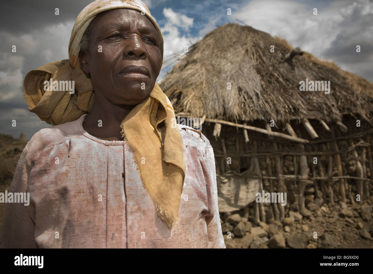 An elderly woman stands in front of her grass and stick home in Kilimanjaro Region Tanzania. Stock Photo