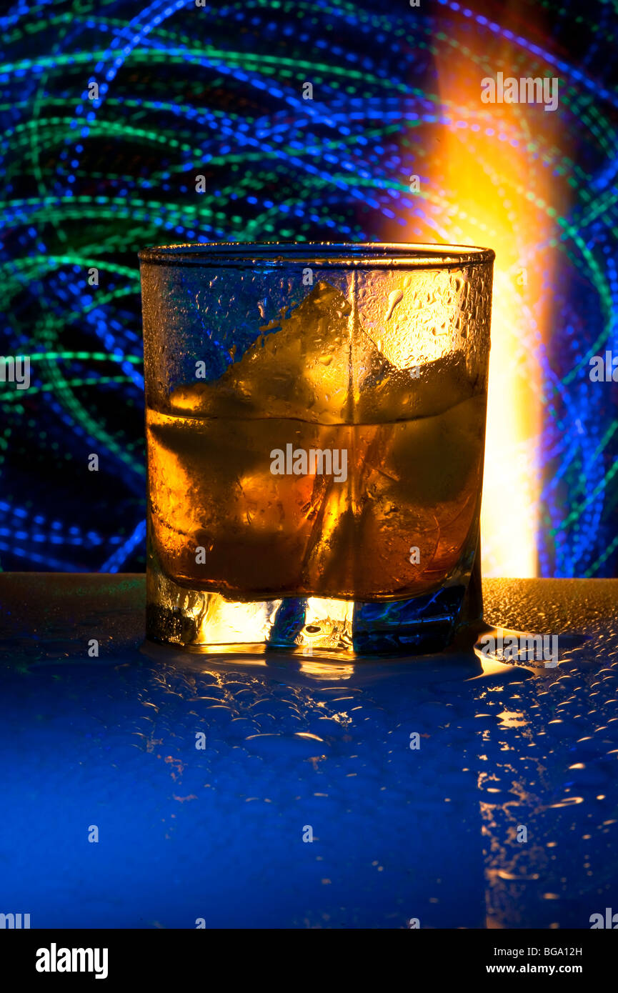 Glass with alcohol against fire with reflexion, in a glass ice. Against a dark background with colour small lamps. Stock Photo