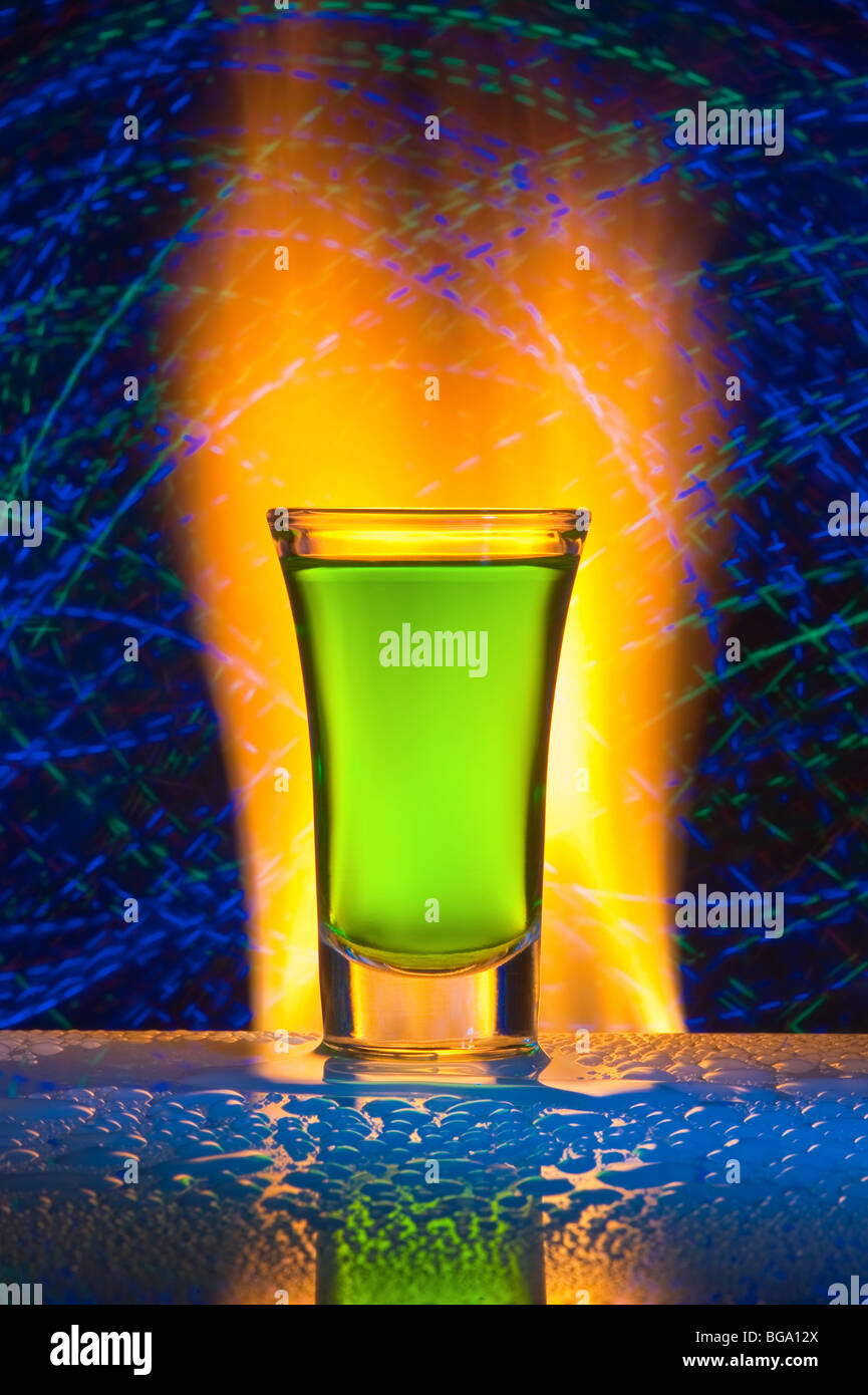 Glass with alcohol against fire with reflexion. Against a dark background with colour small lamps. Stock Photo