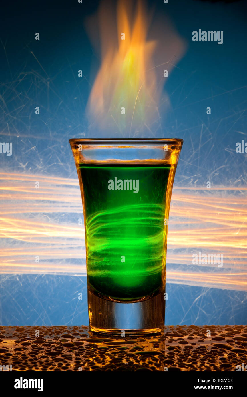 The wine-glass for a cocktail with alcohol of green colour against Bengal fires with reflexion, in a glass burns fire. Stock Photo