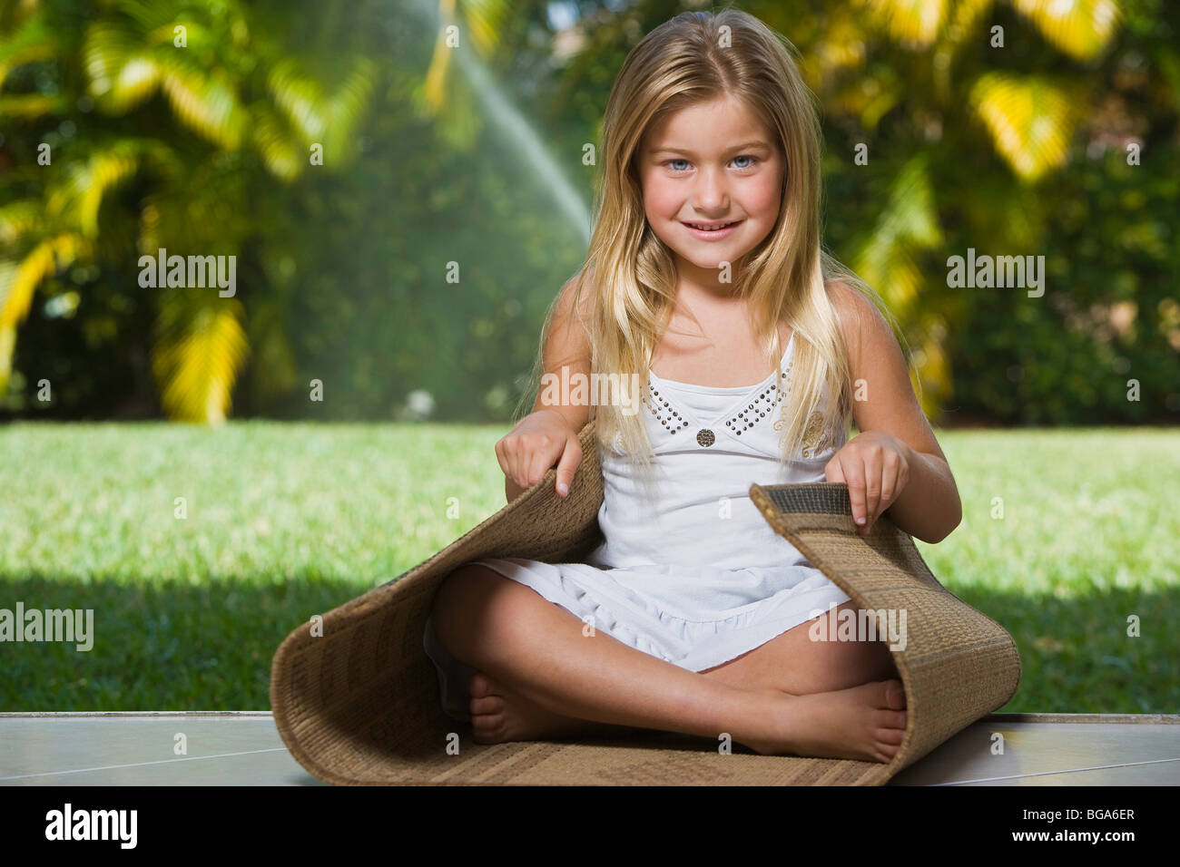 Blond girl sitting down on rug, smiling, portrait Stock Photo