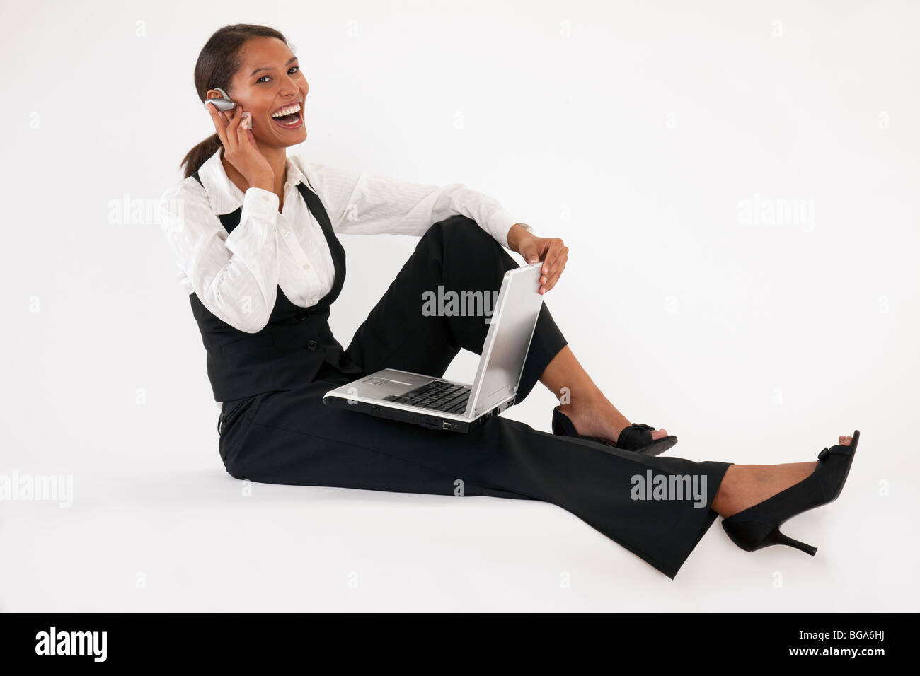 Young woman sitting on floor using laptop and wearing bluetooth headset. Horizontally format. Stock Photo
