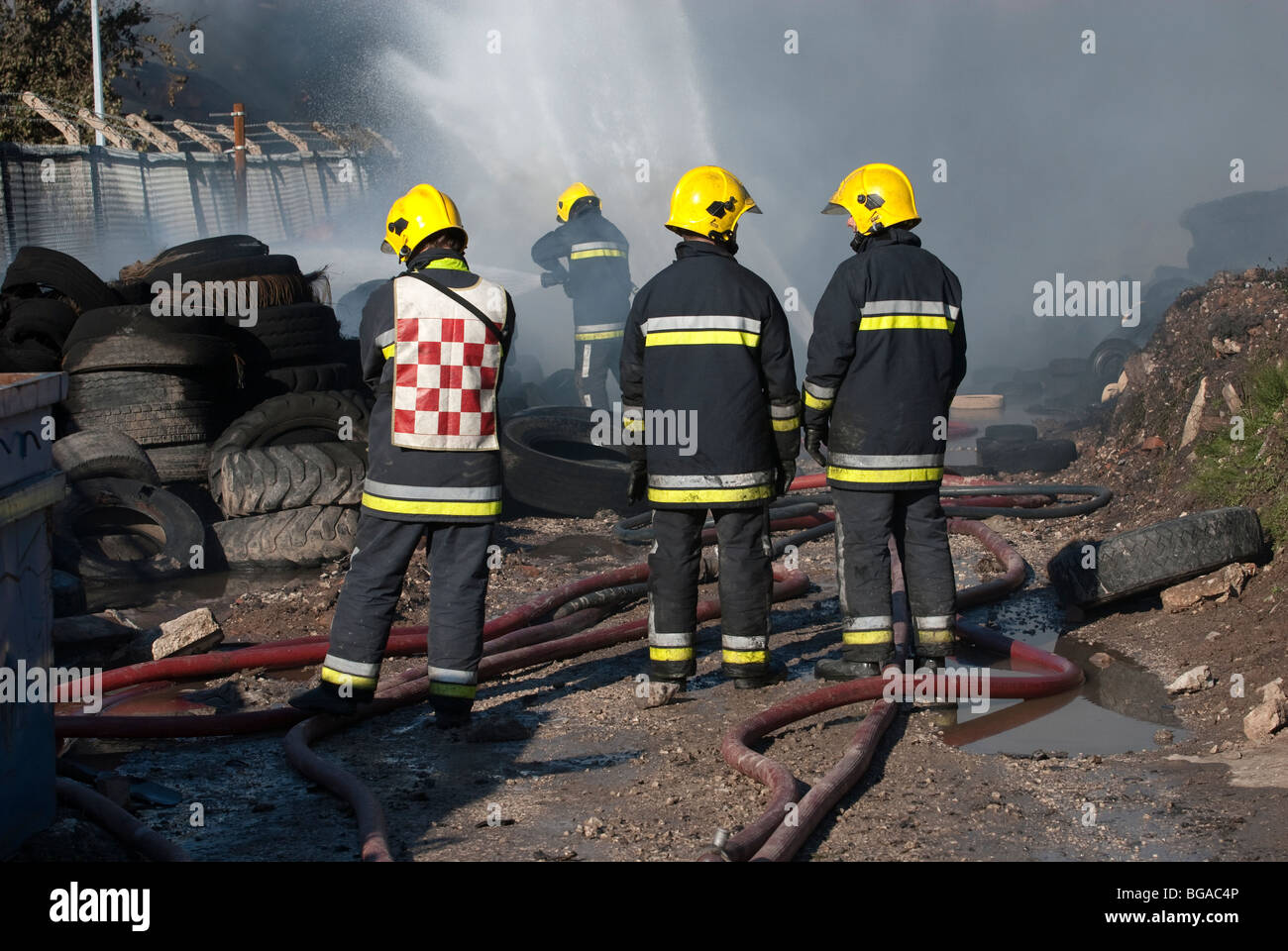 Firemen damping down at pile of tyres on fire Stock Photo