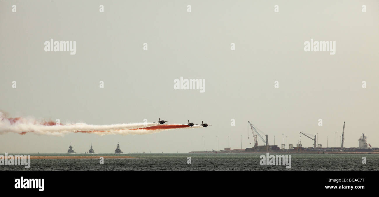 Qatari warplanes trailing national colours of white and maroon fly low past Doha Port, while three Qatari warships head off Stock Photo