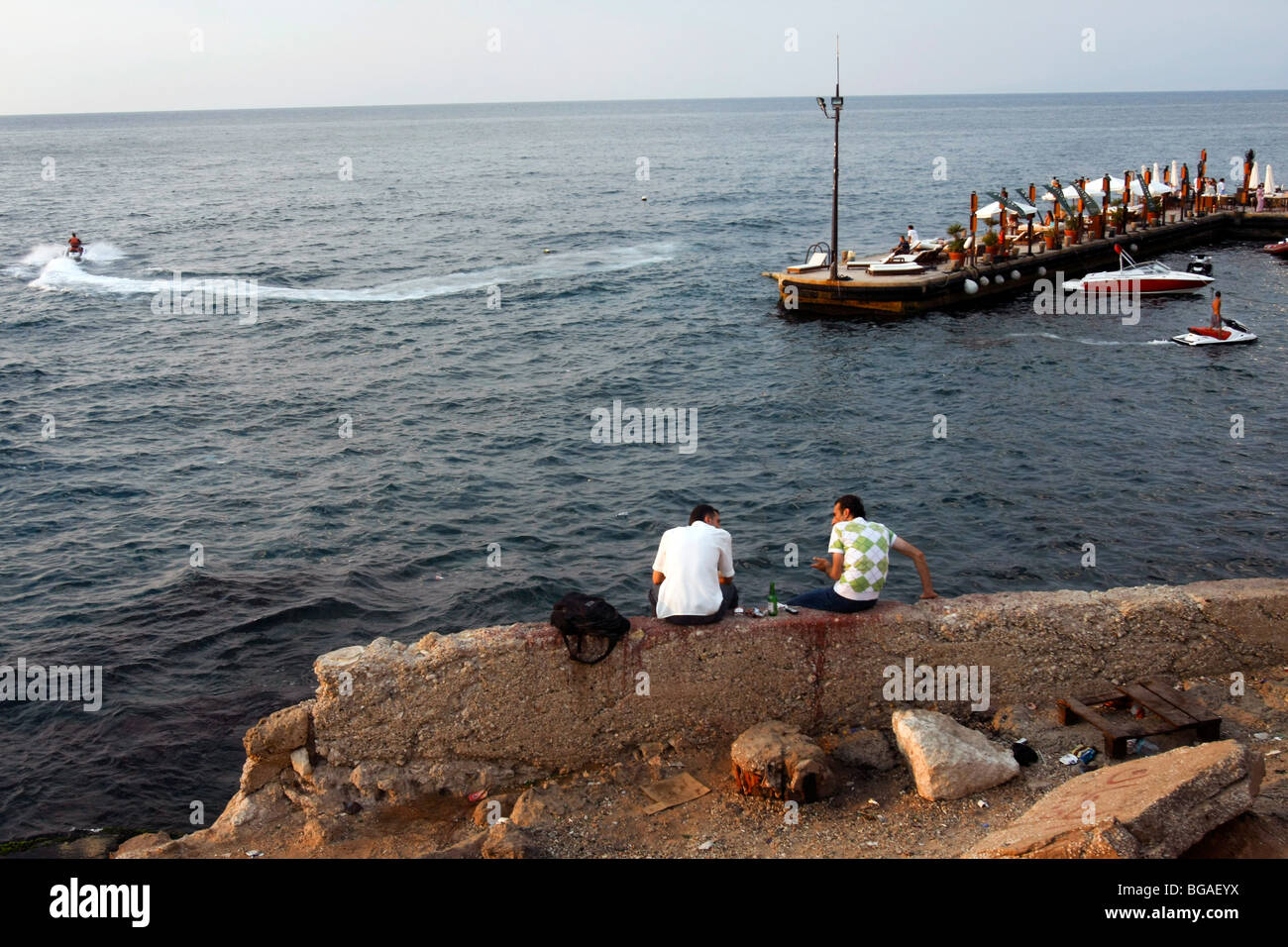 Two men sit along the sea shore near the Cornich sea side promenade in Beirut in Lebanon. Stock Photo