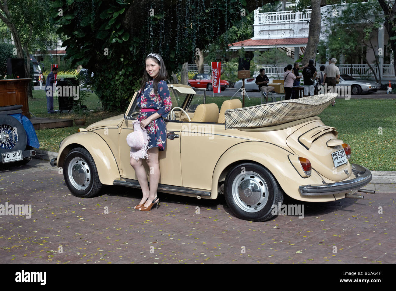 Female model posing with a classic cream Volkswagen Beetle convertible motor car. Thailand S. E. Asia Stock Photo