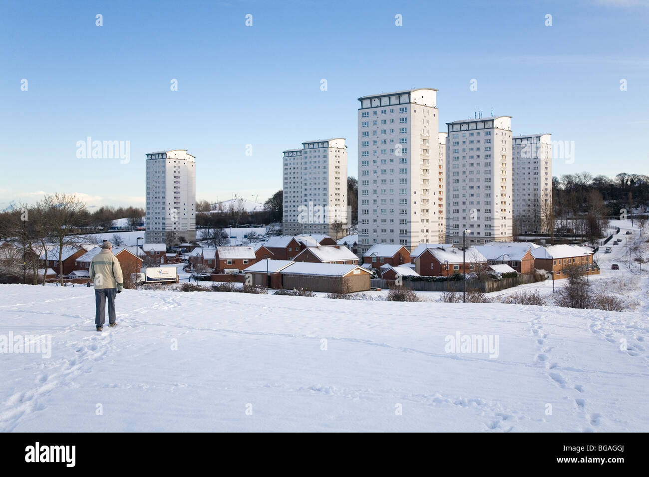 A man walks through snow in Sunderland, England. The high-rise Gilley Law housing estate can be seen in the background. Stock Photo