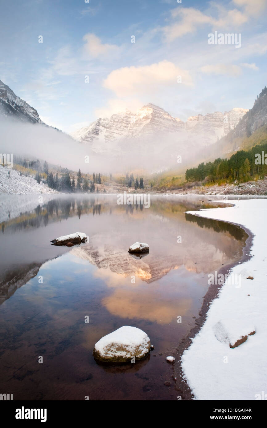 Maroon Bells (in the background) in the morning mist with lake, snow and ice formation in the foreground. Stock Photo