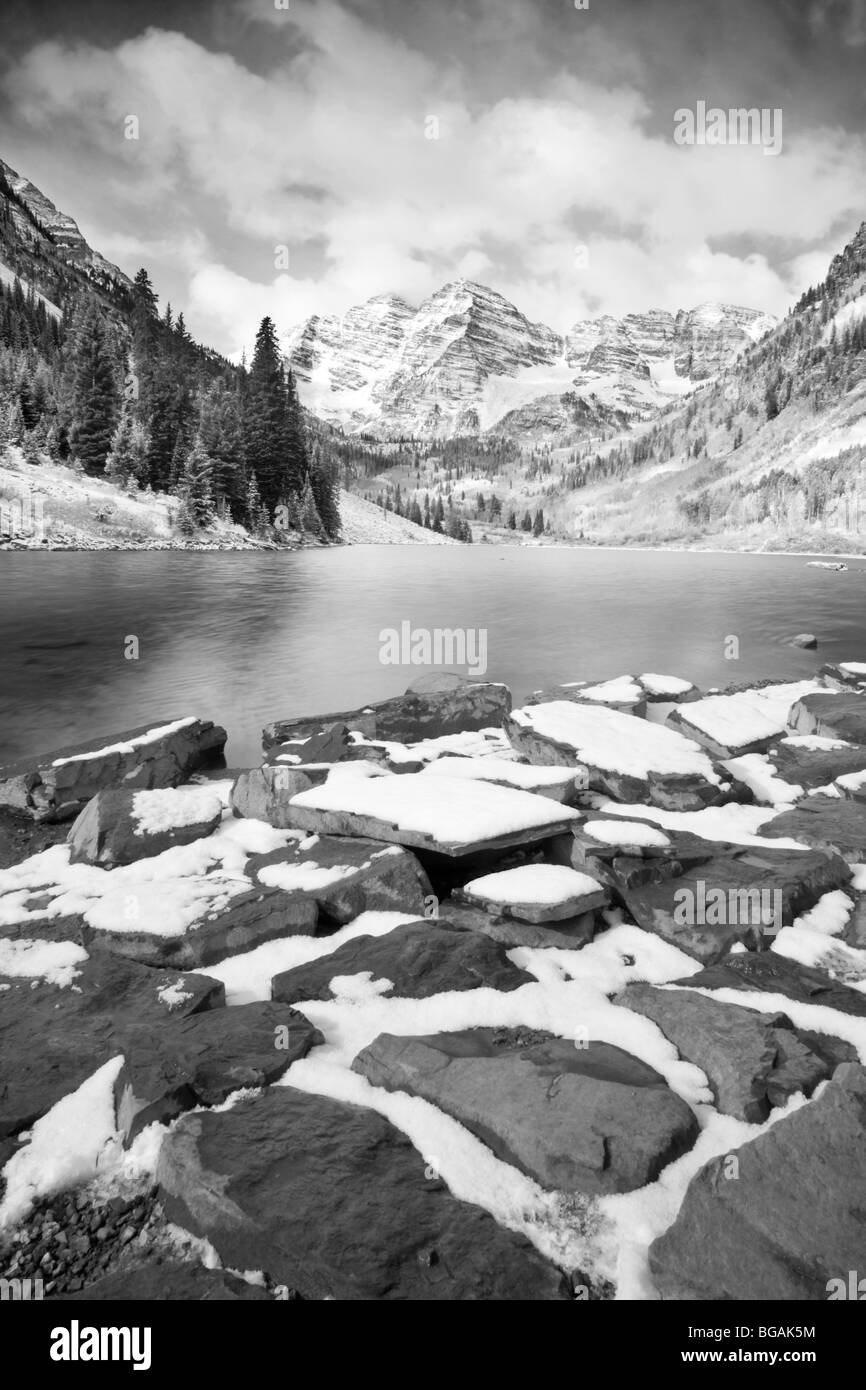 Maroon Bells in the background and large stones with snow along the shores of the lake. Cloudy sky and black and white image Stock Photo