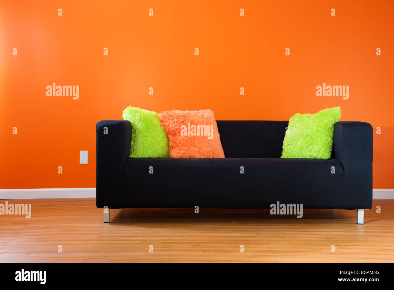 Contemporary black couch against bright orange wall in a modern living room Stock Photo