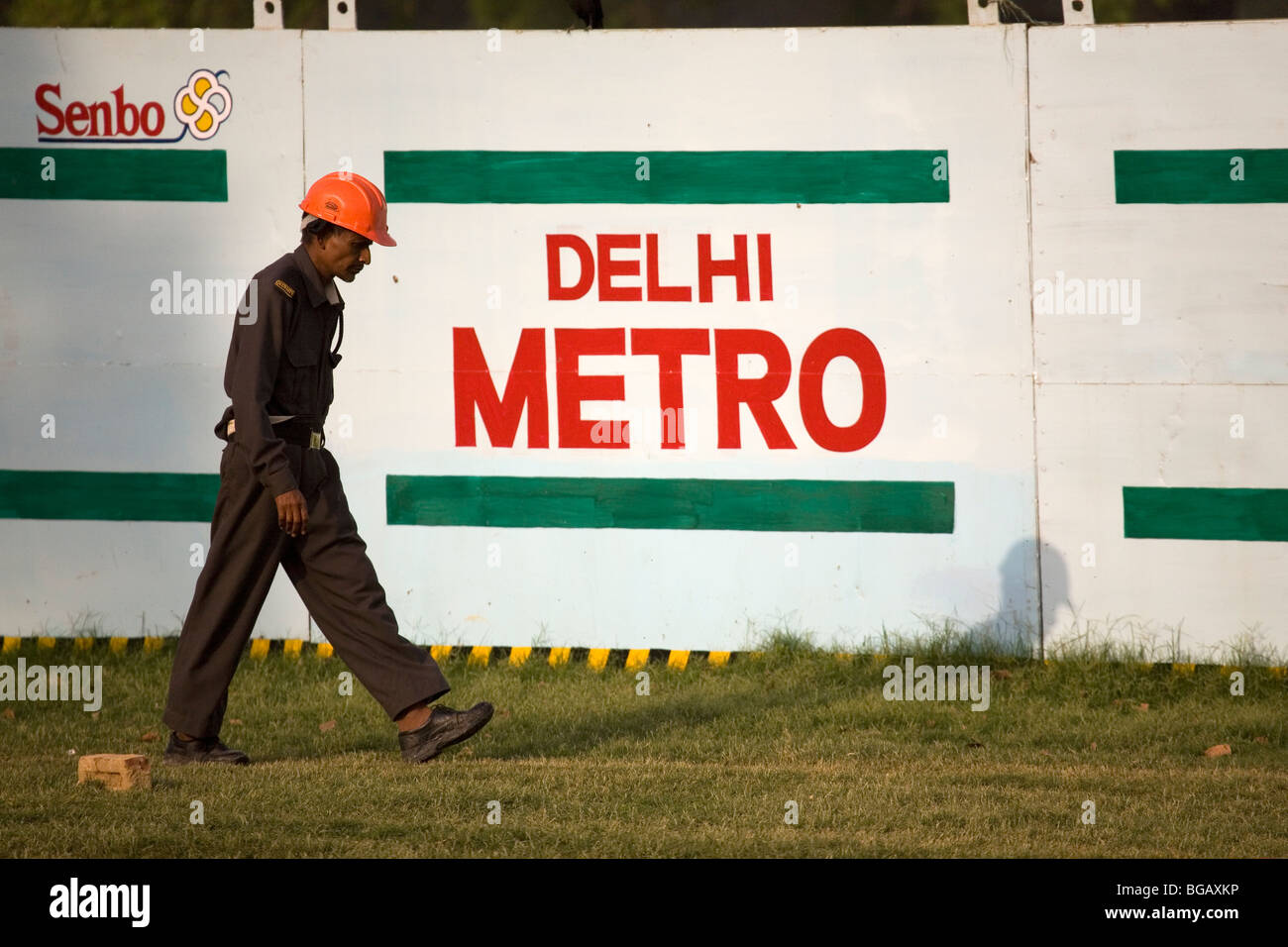 A man in a safety helmet walks in front of a board saying Delhi Metro in New Delhi, India. Stock Photo