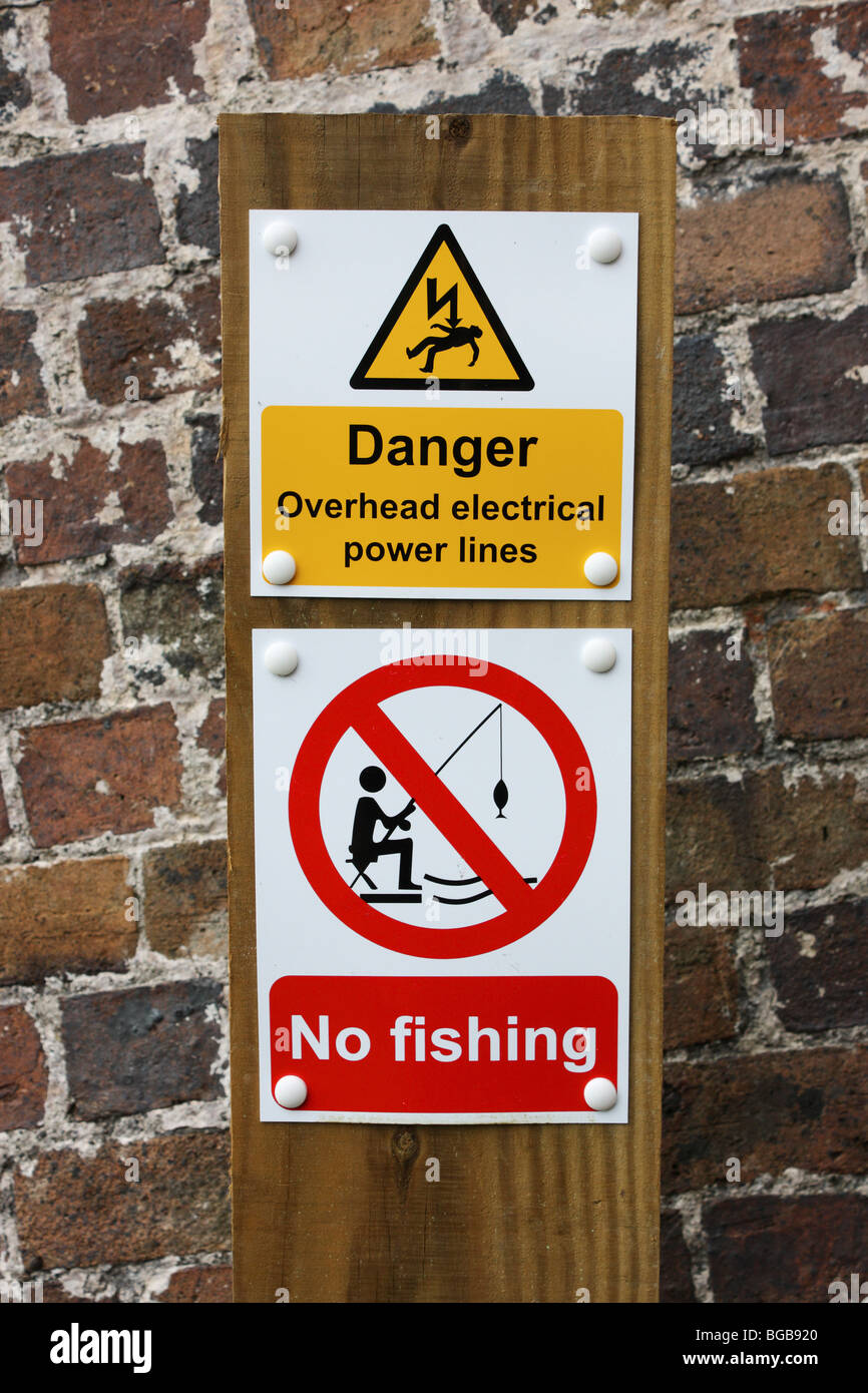 Signs warning anglers that there is no fishing along a stretch of canal due to overhead power lines Stock Photo