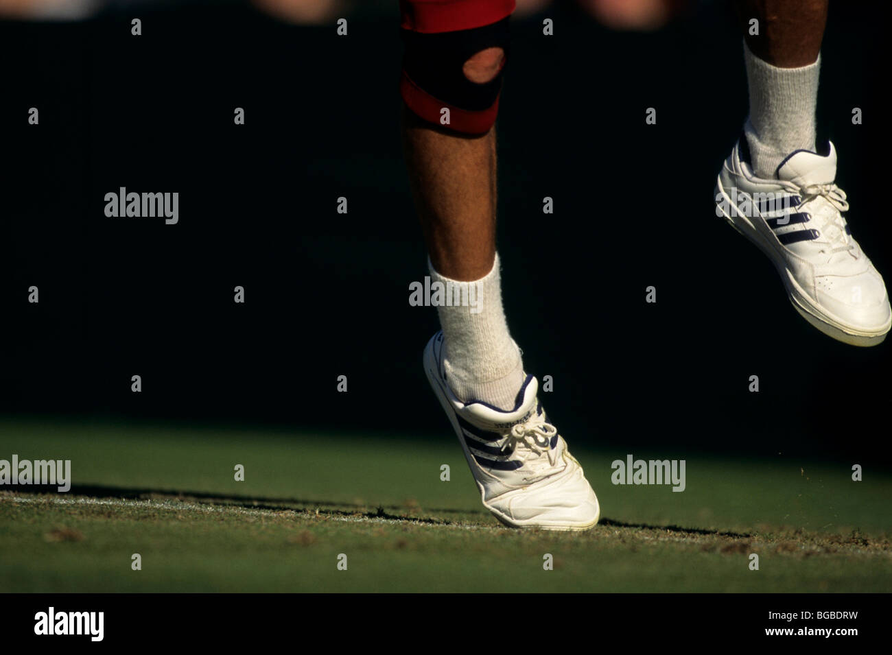 Tennis player wearing a knee brace serving a ball at the service line Stock Photo