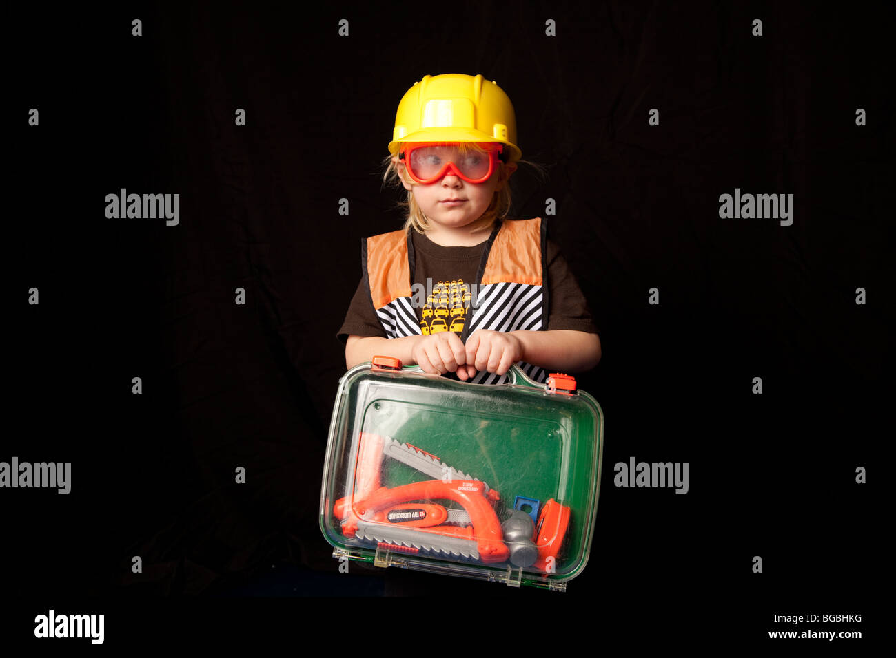 4 to 6 year old child in construction worker costume, holding a plastic tool box with tools in it. Stock Photo