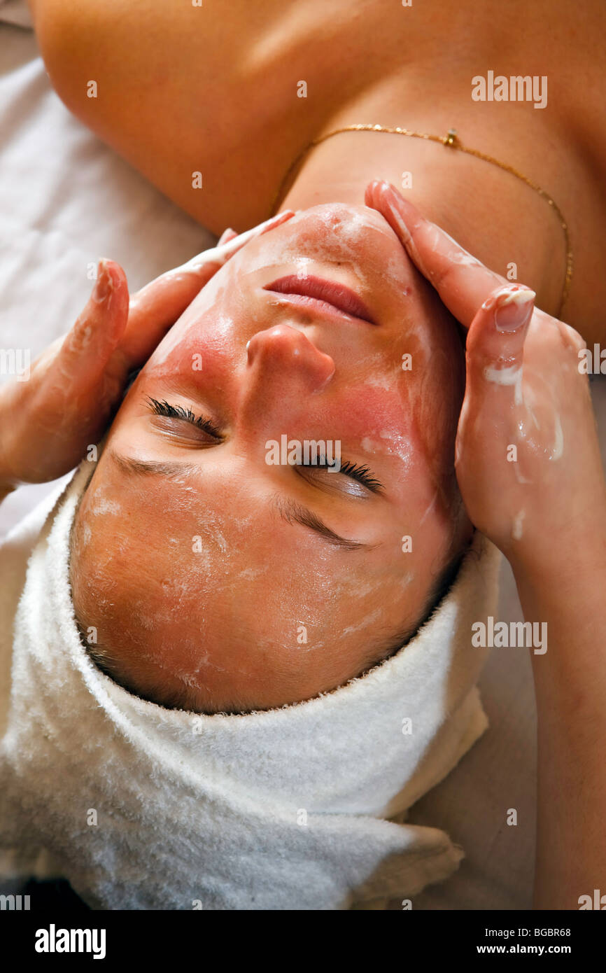 Therapist applying lotion to the face of a young woman during a relaxing facial treatment. Stock Photo