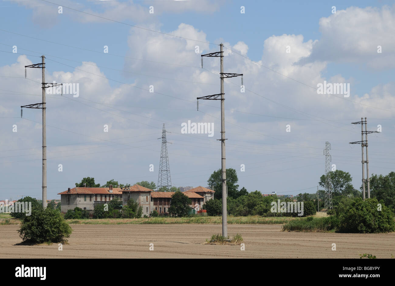 High voltage power cables wires and pylons crossing farm land in the foreground Southern periphery of Milan Lombardy Italy Stock Photo