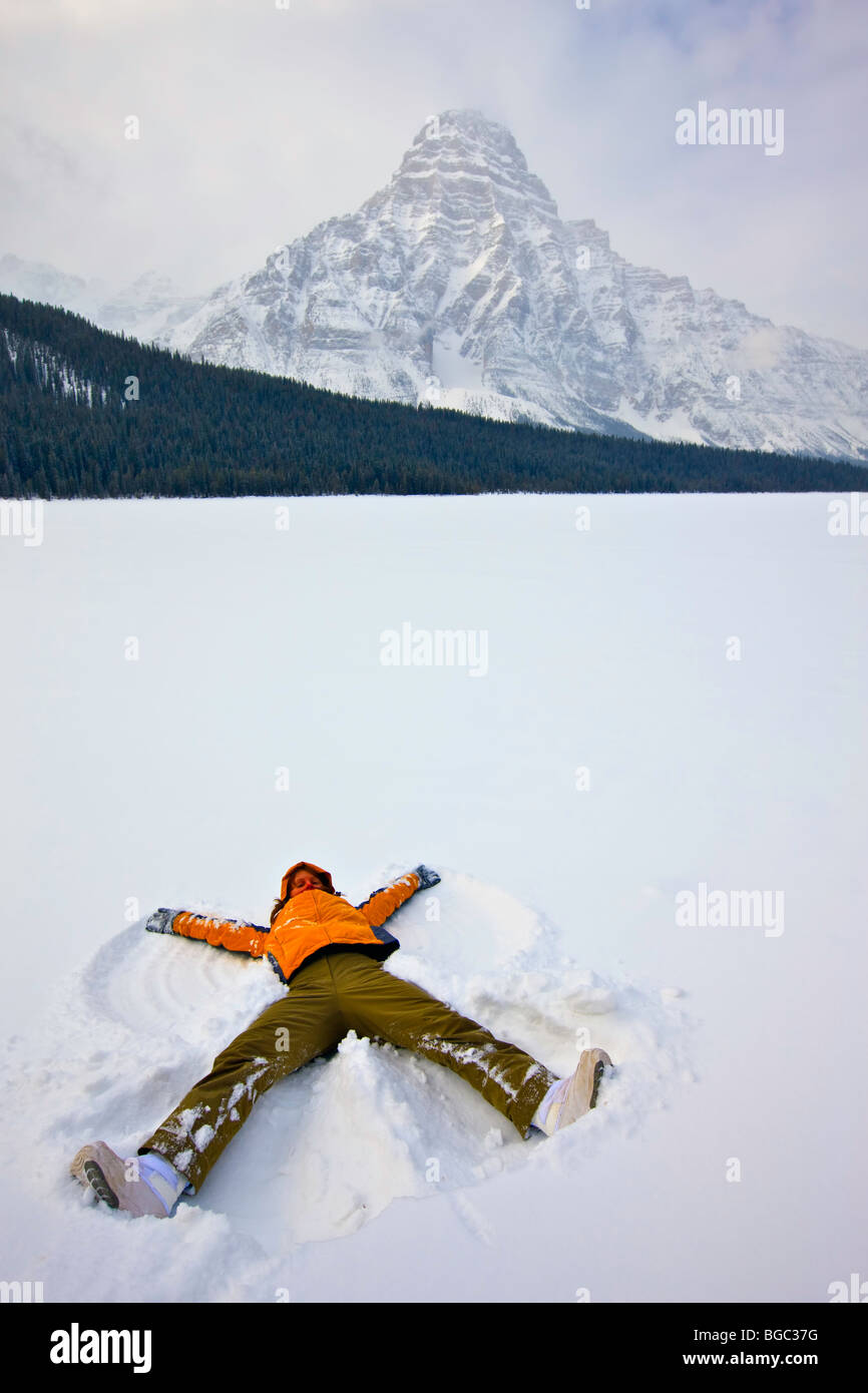 Woman making a snow angel on Waterfowl Lake after fresh snowfall during winter with Mount Chephren (3307 metres/10850 feet) towe Stock Photo