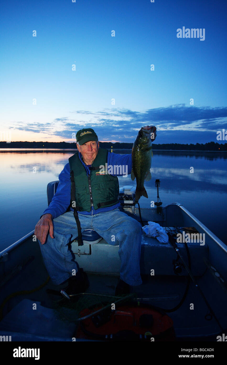 senior elderly fishing guide fisherman holding up monster five 5 pound largemouth bass sitting in boat sunsrise Stock Photo