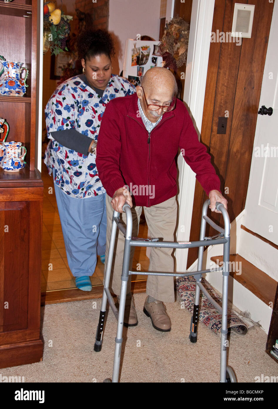 Home health care worker helps elderly man use his walker. Stock Photo