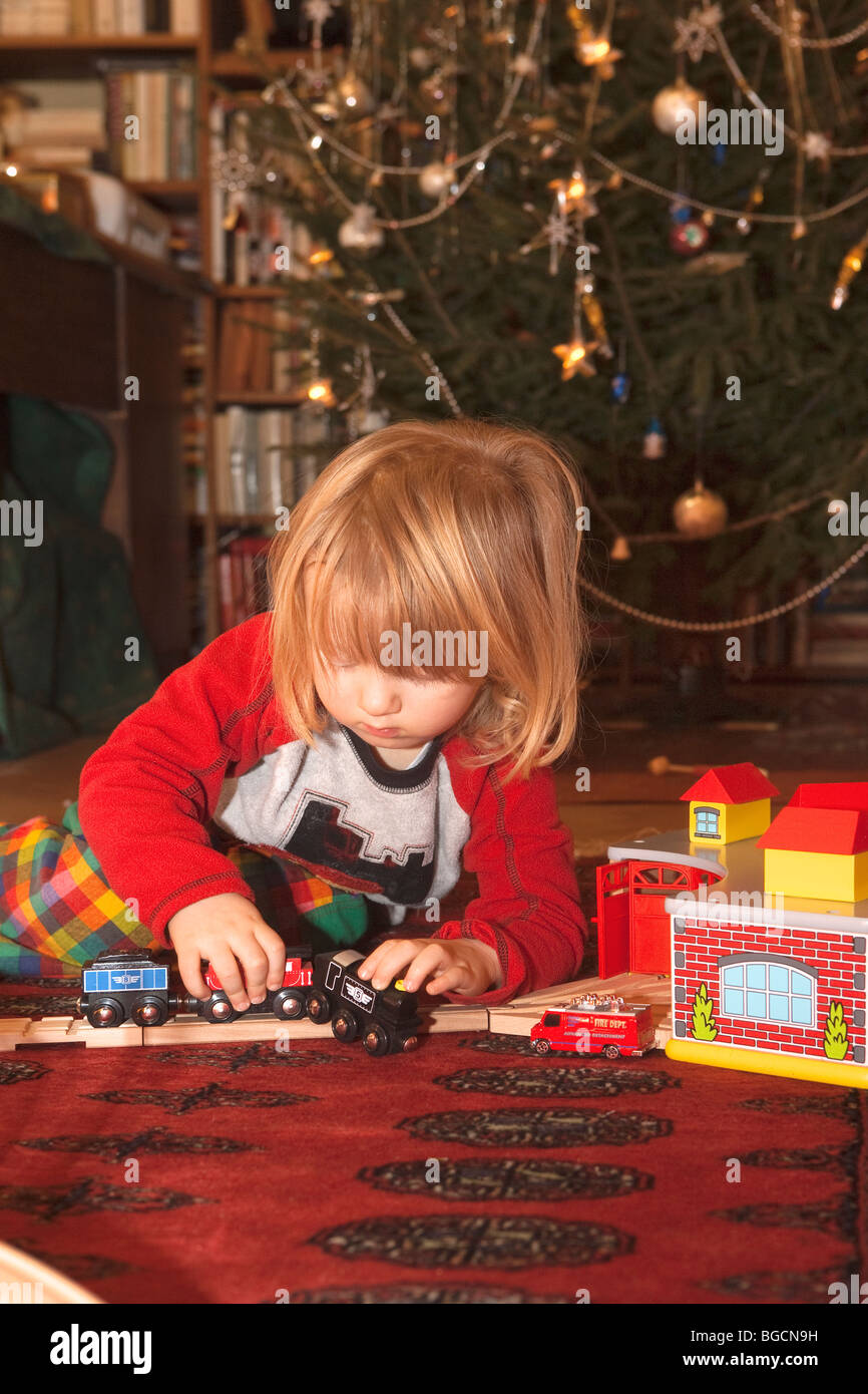 boy playing with toy train in front od christmas tree