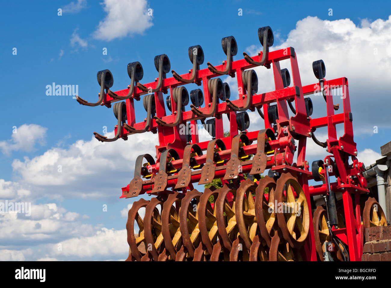 Bright red farming implement, against bright blue sky and white clouds Stock Photo