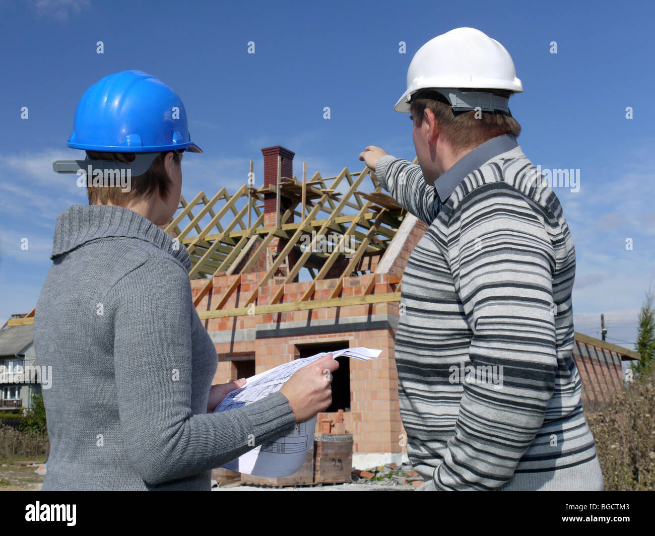 Female and male building engineers wearing helmets discussing building plans over unfinished brick house Stock Photo