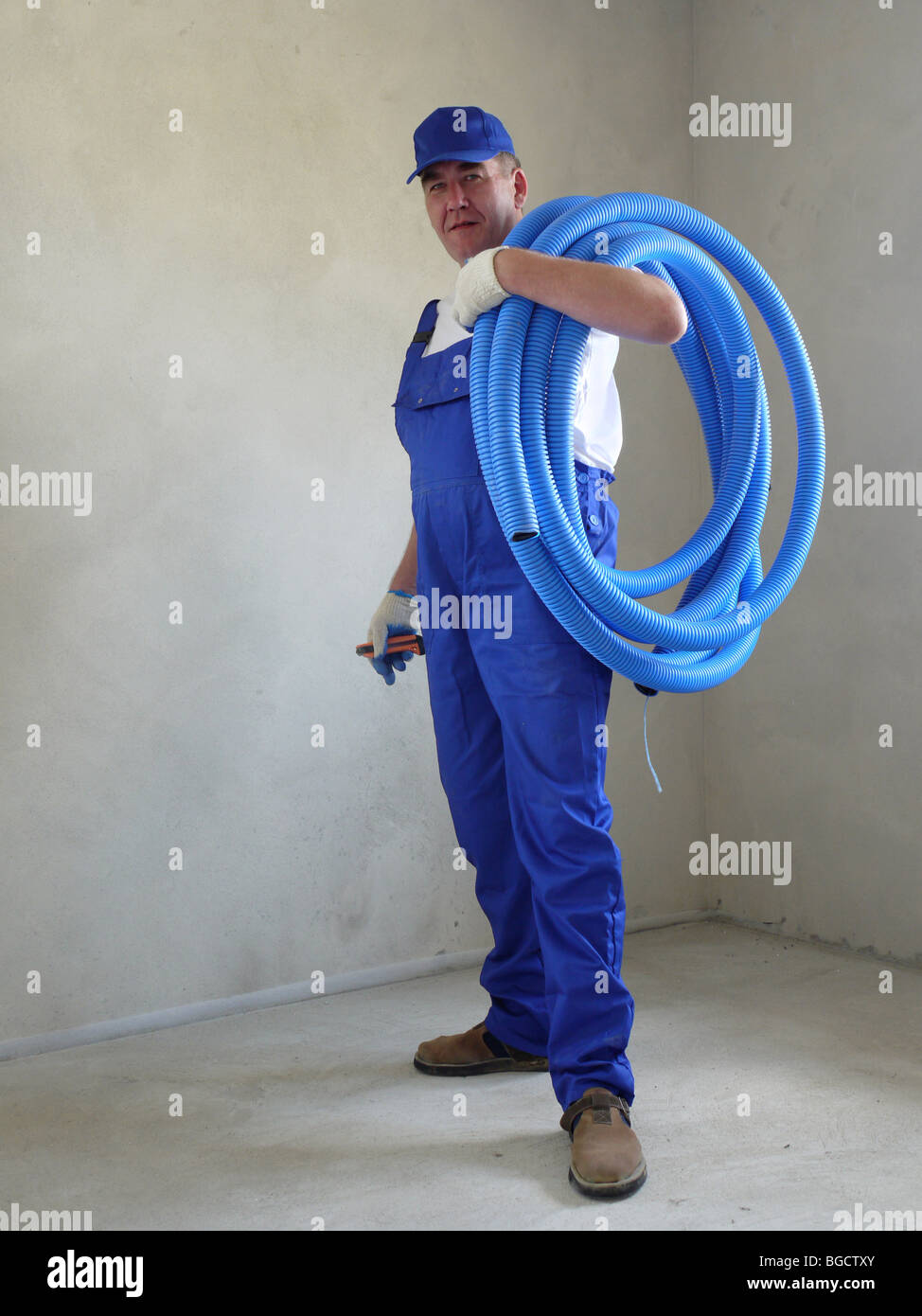 Electrician wearing white shirt, blue cap and blue uniform posing with coil of PVC flexible corrugated cable protection pipe Stock Photo