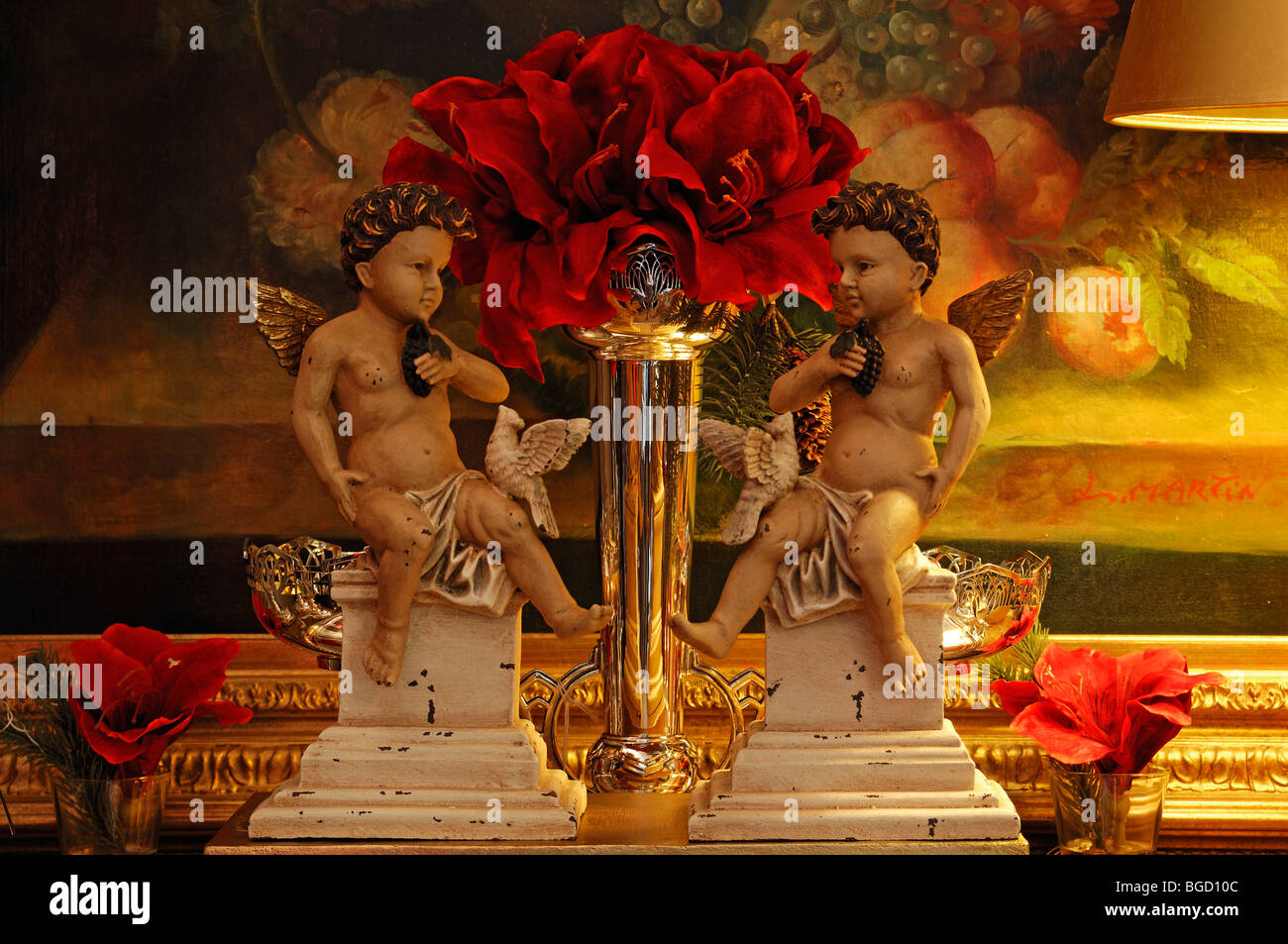Two cherubs sitting on pillars and a silver vase with a red amaryllis in front of a painting, Villa & Ambiente store, Im Weller Stock Photo