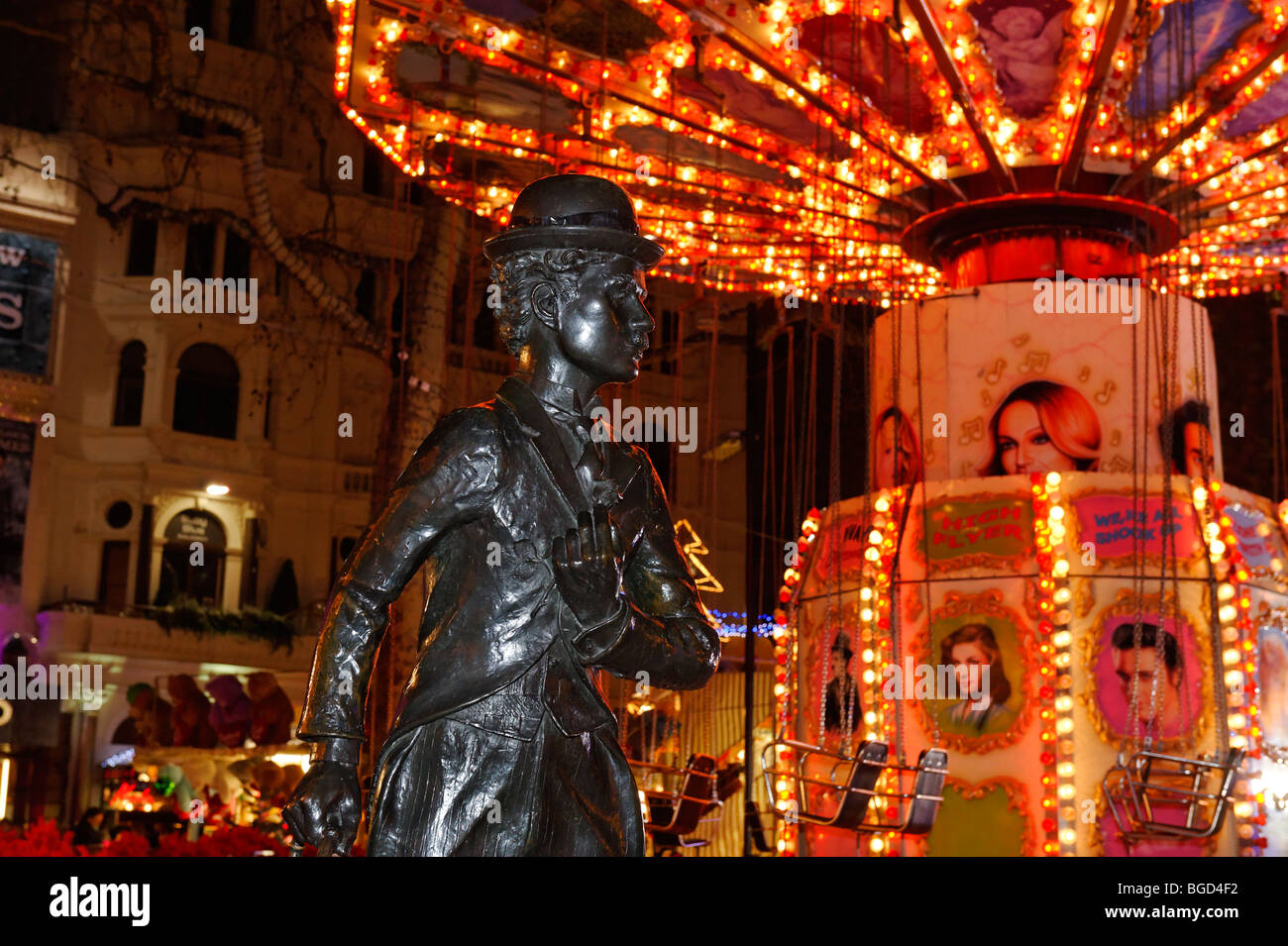 The statue of Charlie Chaplin in Leicester Square with a bright fairground ride behind. Stock Photo