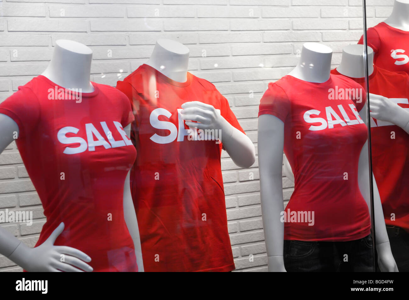 Mannequins behind glass with a sale sign on their red T-shirts. Stock Photo