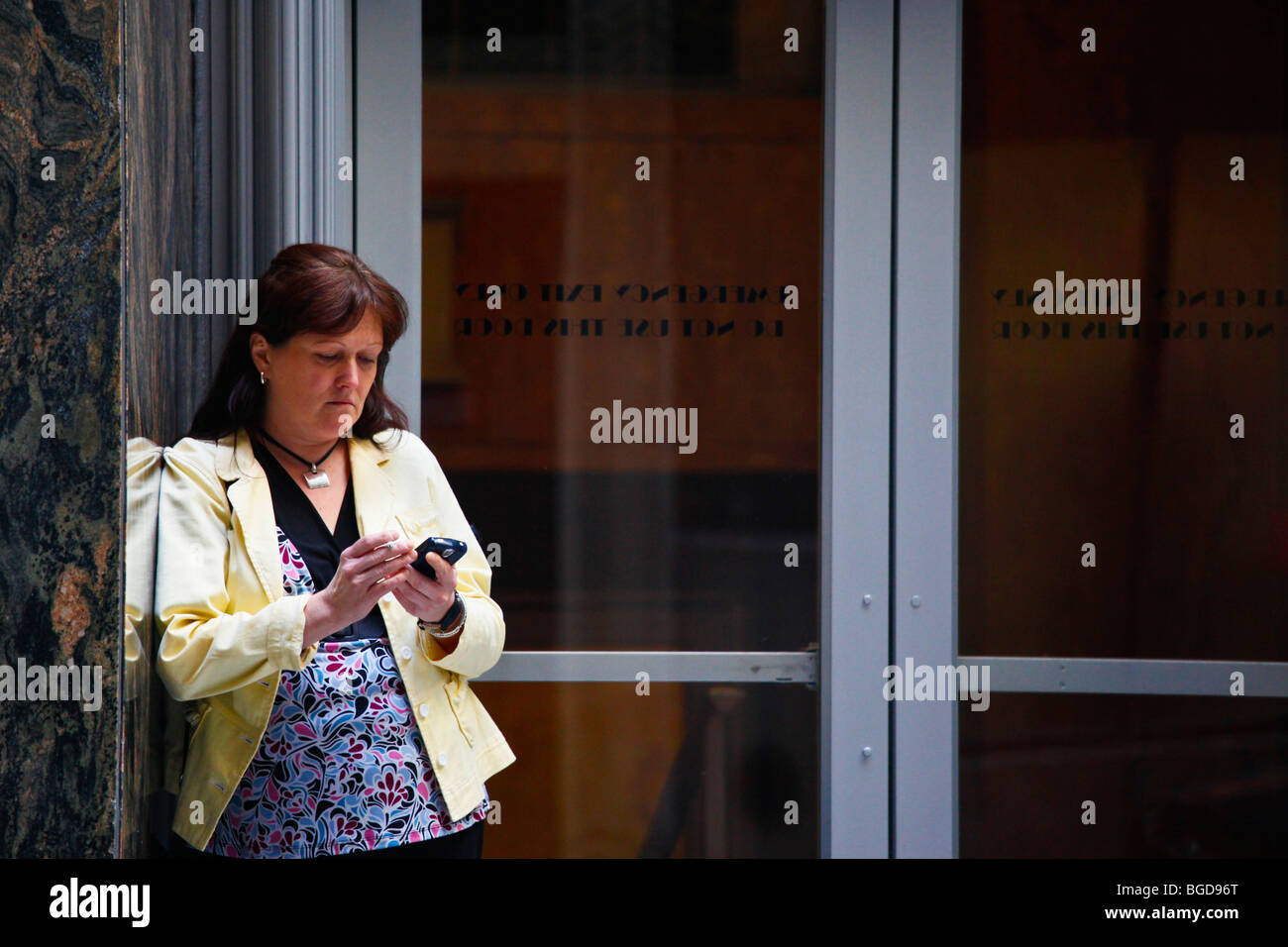 Woman using a blackberry and smoking outside a building in downtown Manhattan, New York City Stock Photo