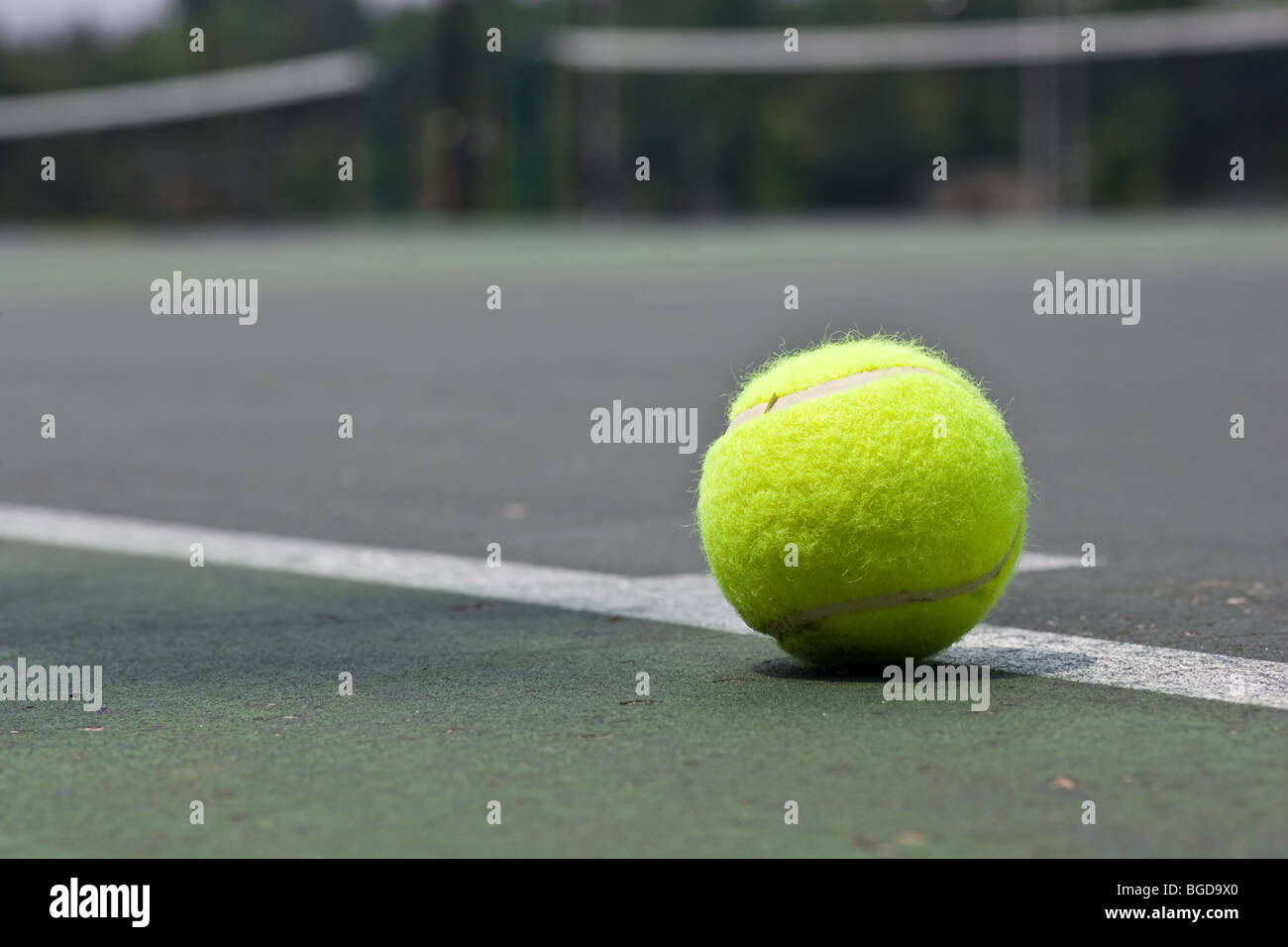 A closeup of a yellow tennis ball just outside of the base line on an asphalt tennis court. Stock Photo