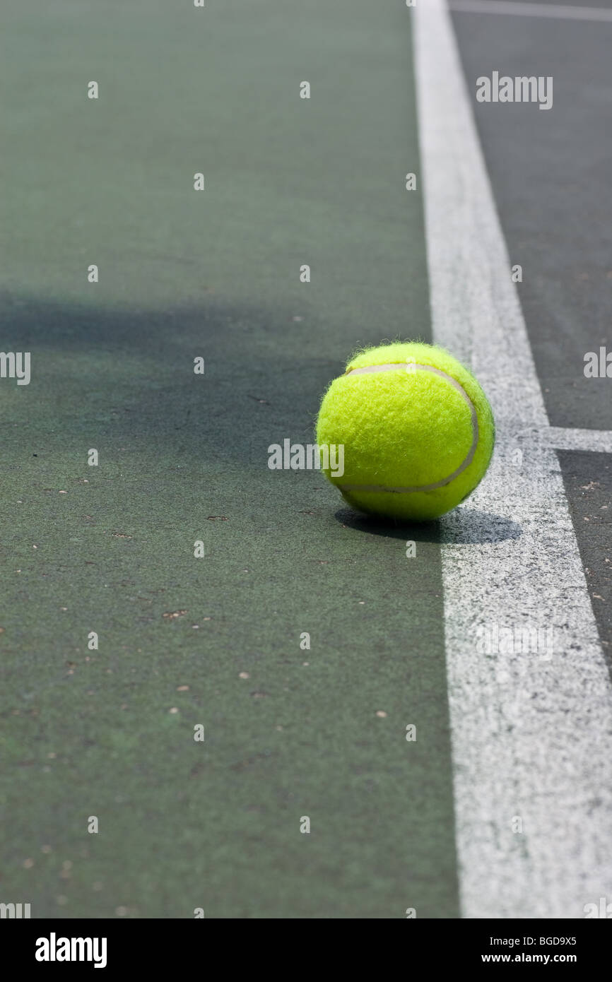 A yellow tennis ball being shown as out, just beyond the base line on an asphalt tennis court. Stock Photo